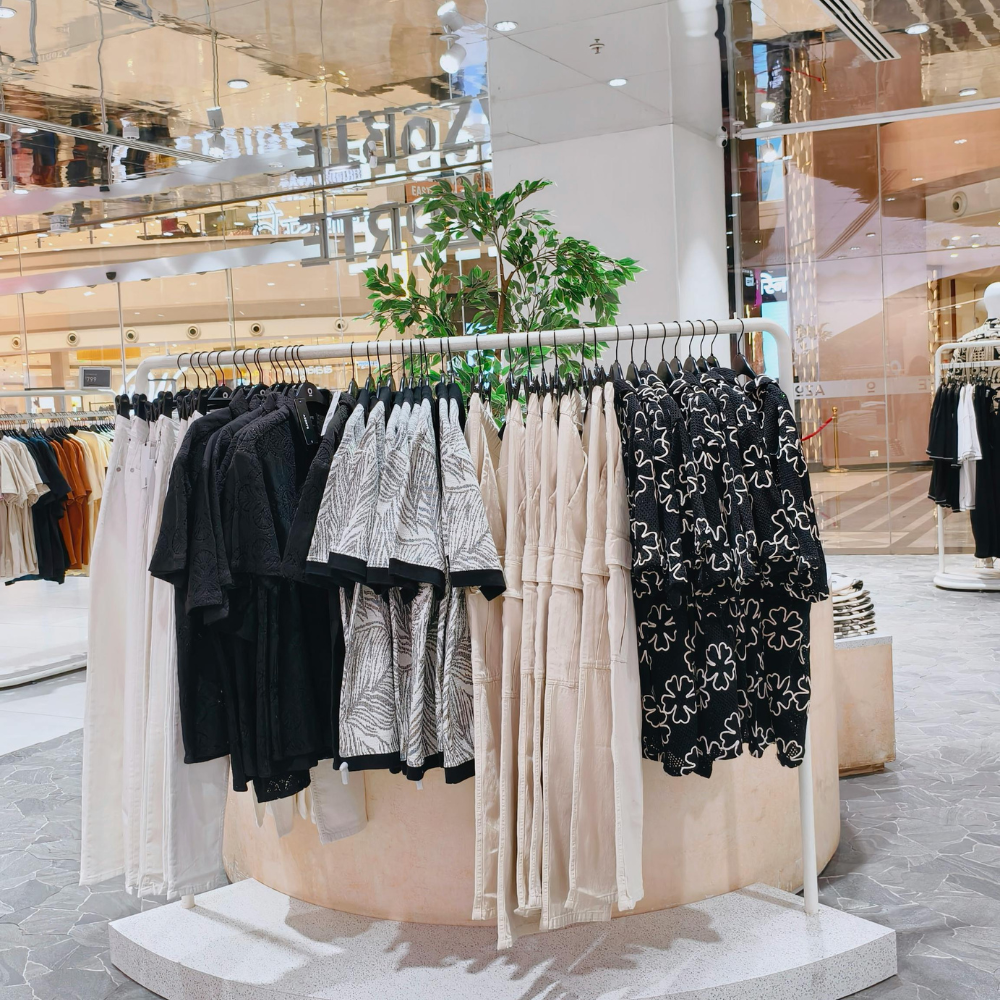 Clothing rack displaying black, white, and beige shirts and pants in a shopping mall.