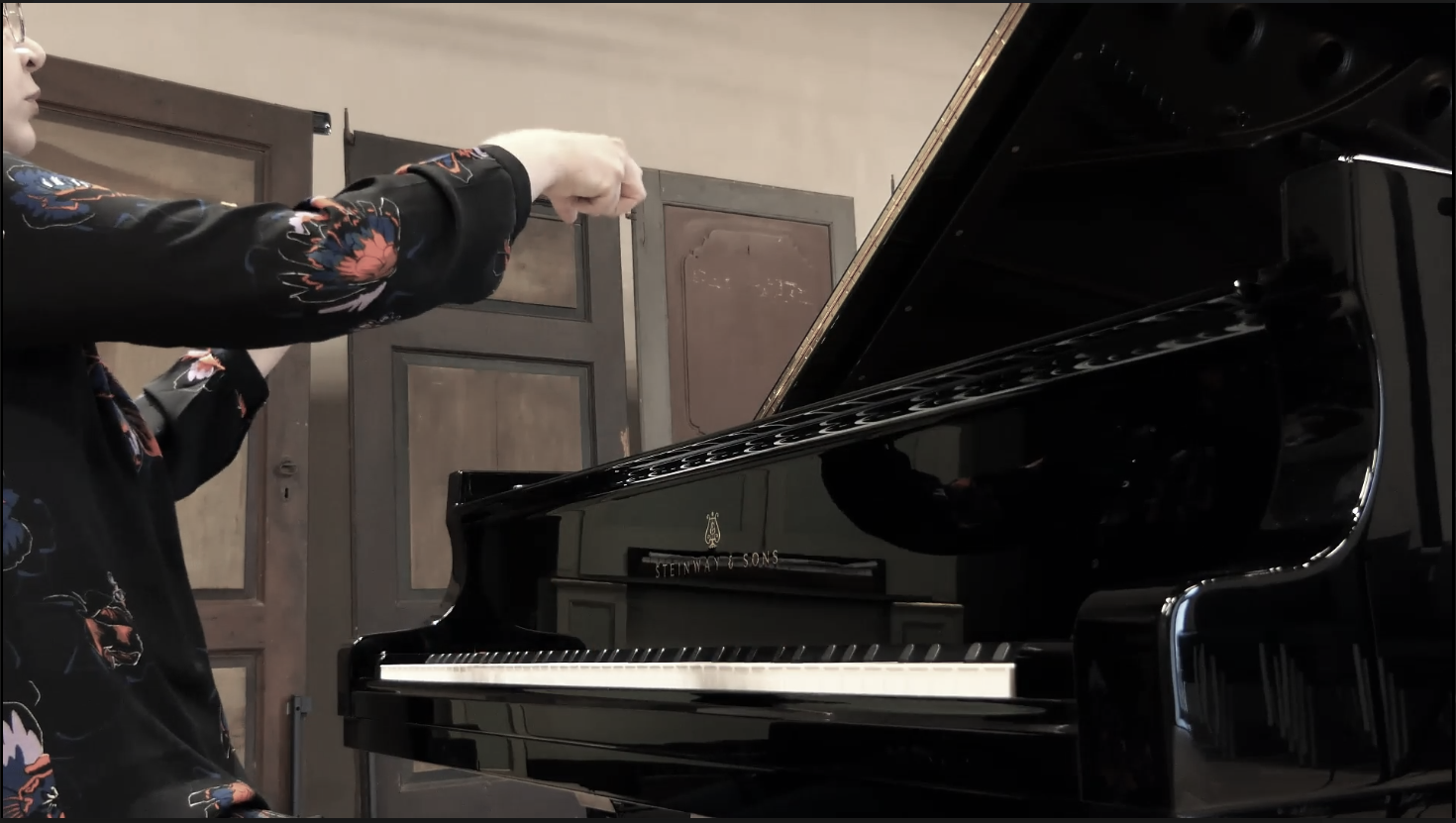 A person playing a black Steinway & Sons grand piano in a room with wooden walls.