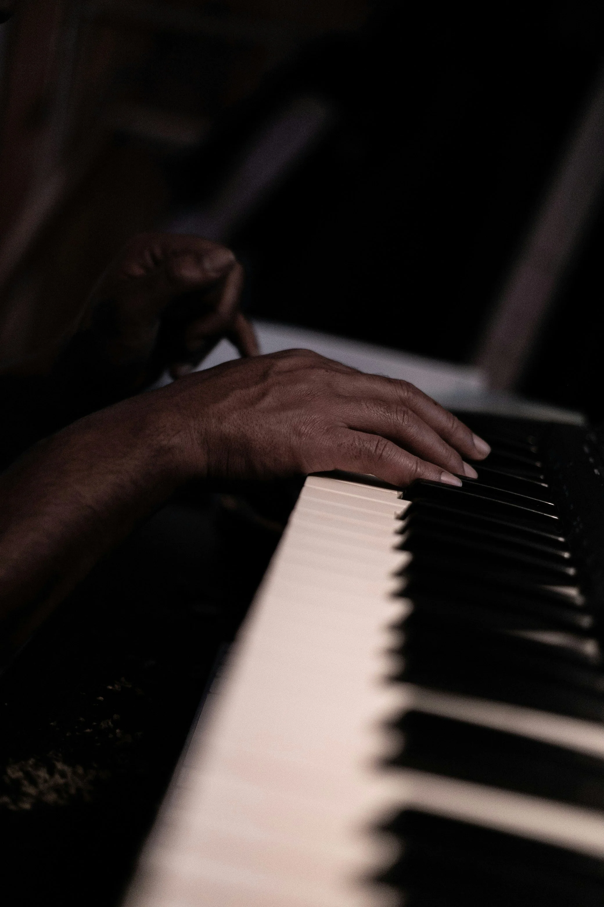 Close-up of hands playing a piano keyboard at night, with a dark background.