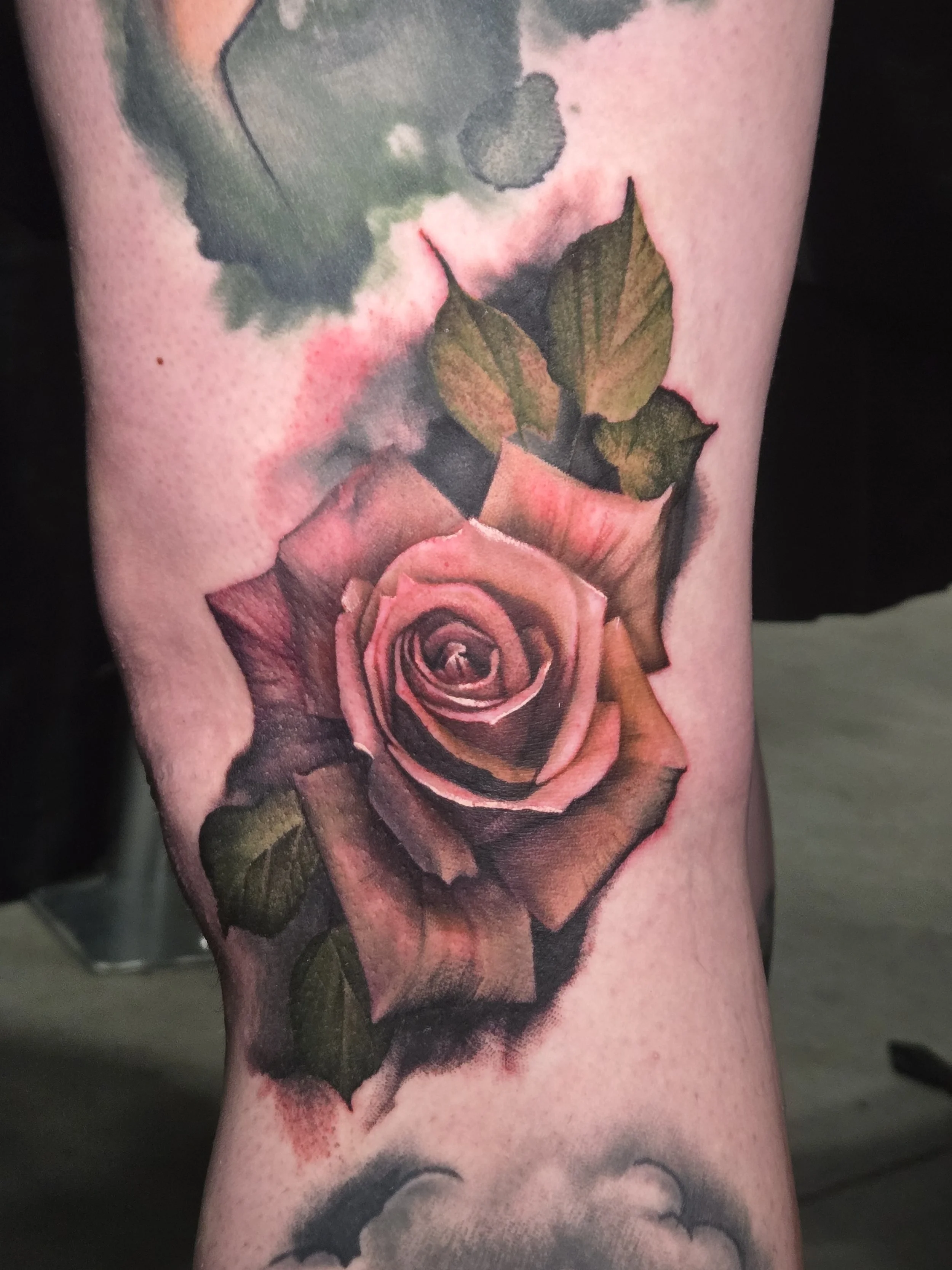 A tattoo of a realistic pink rose with green leaves on person’s arm.