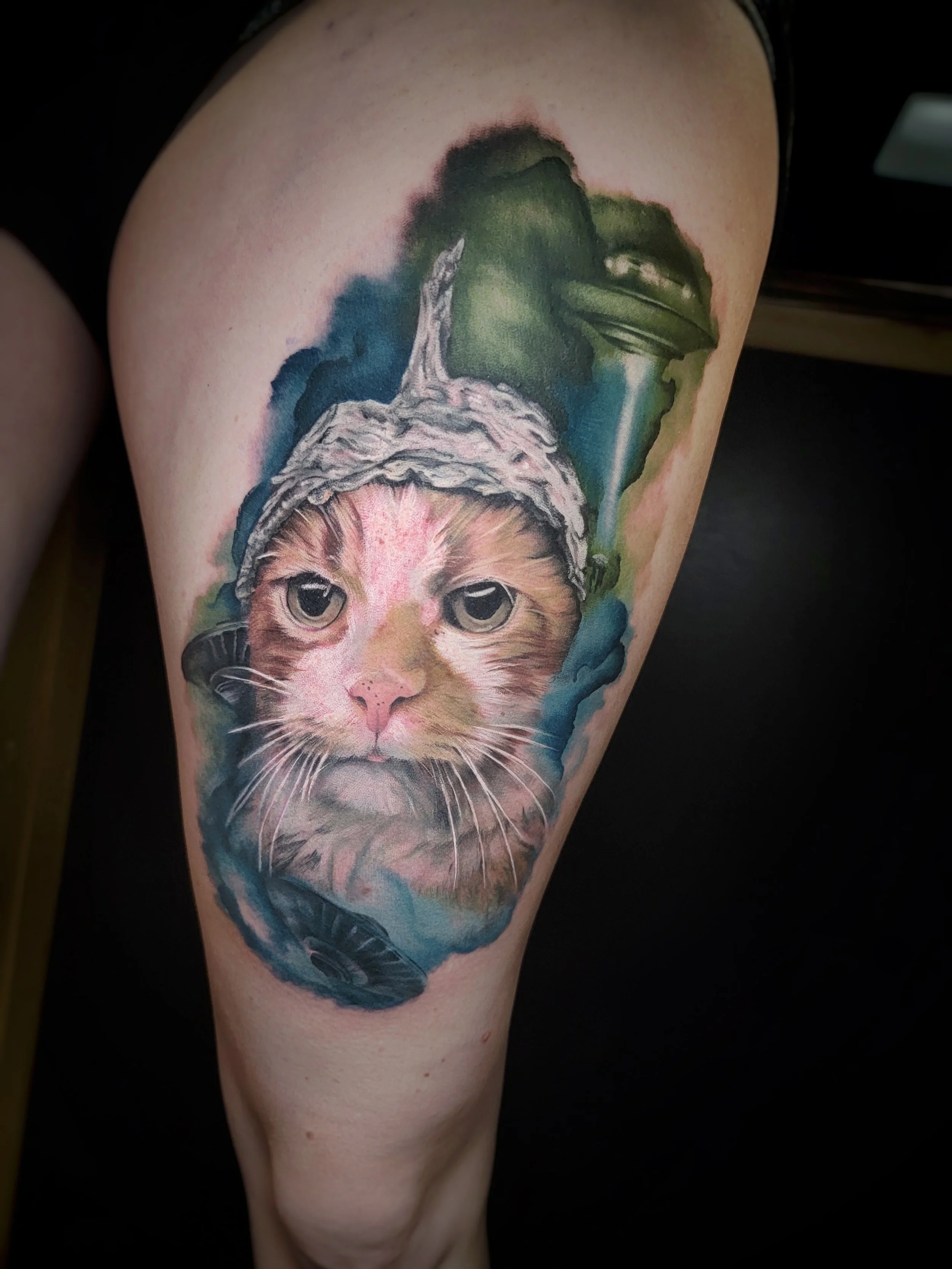 Tattoo of a cat wearing a tin foil hat on a person's thigh.