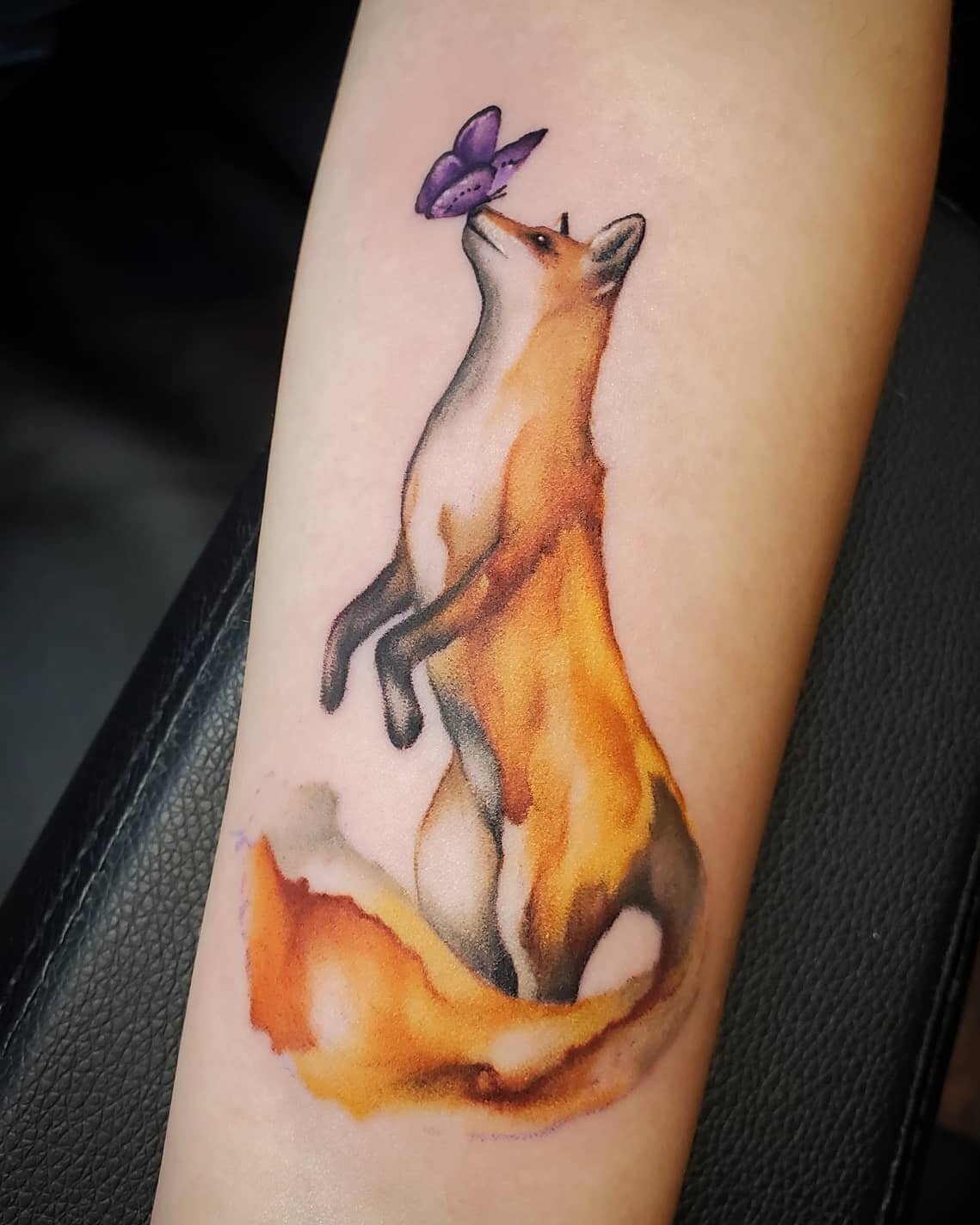 A tattoo of a sitting fox with a purple butterfly above its nose.
