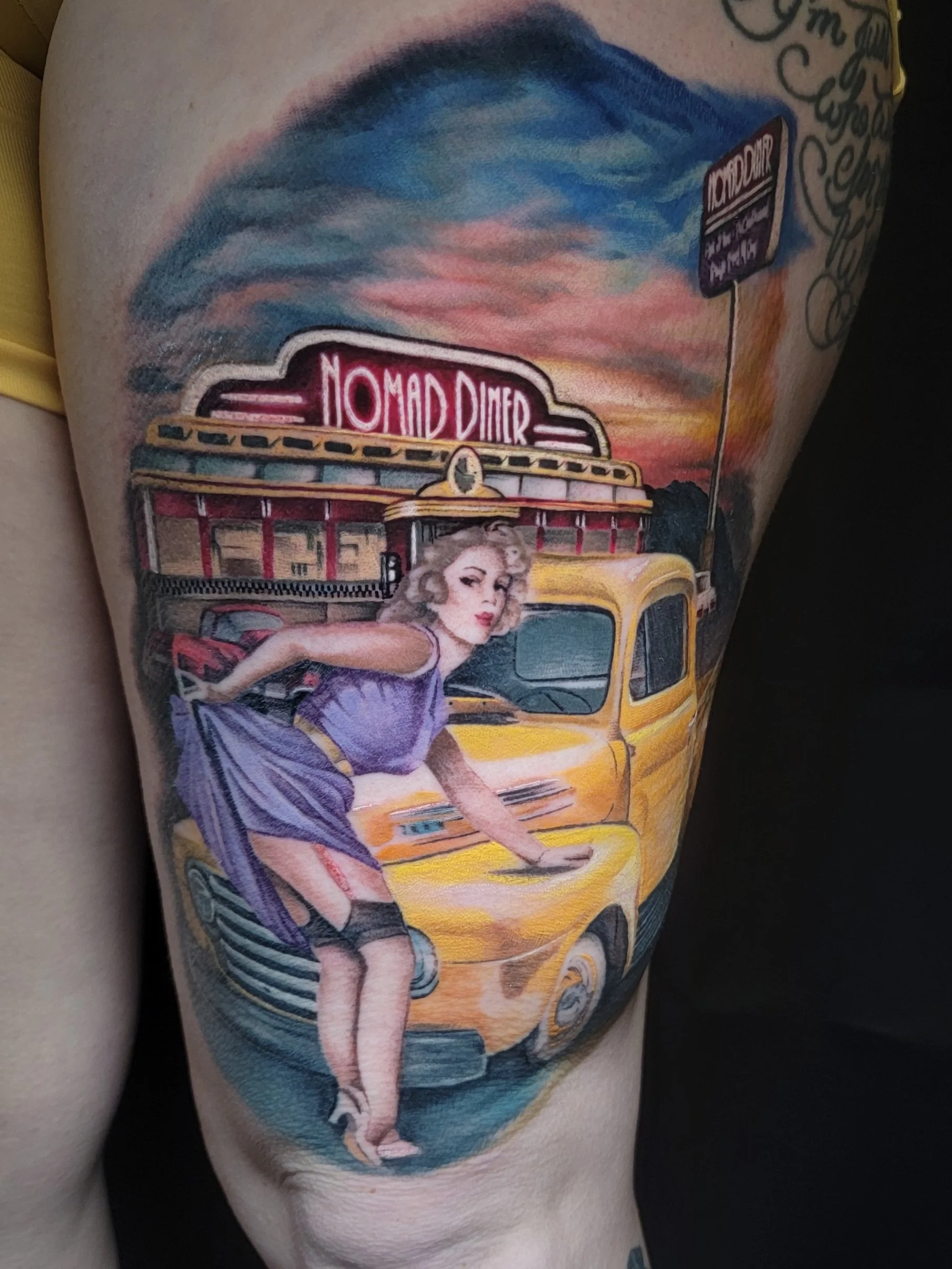 A tattoo depicting a retro-style scene with a woman in a purple dress leaning on a yellow vintage car in front of a diner with neon signs, a sunset sky, and a street sign, on the person's thigh.