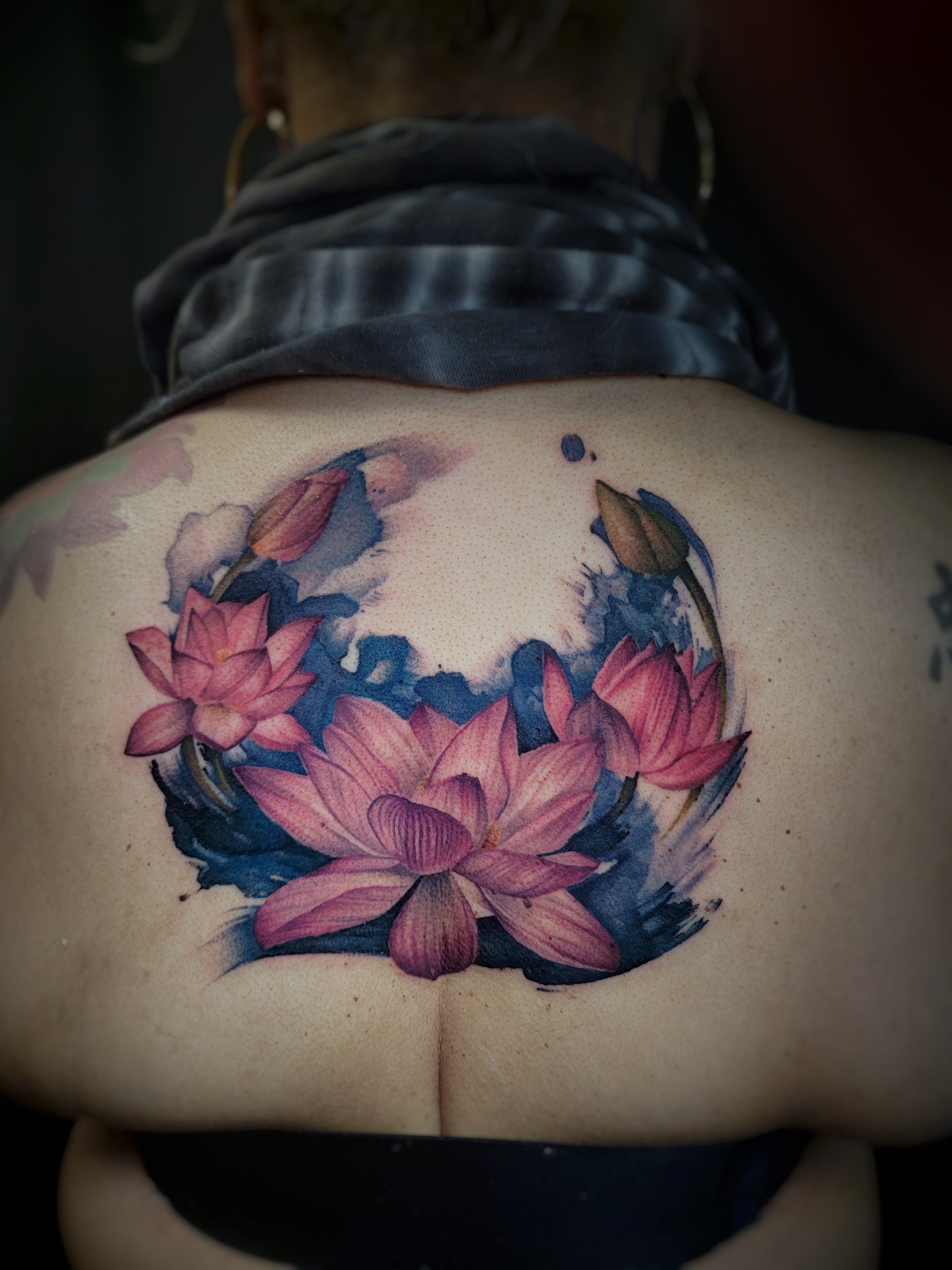 Close-up of a person's upper back with a colorful lotus flower tattoo.
