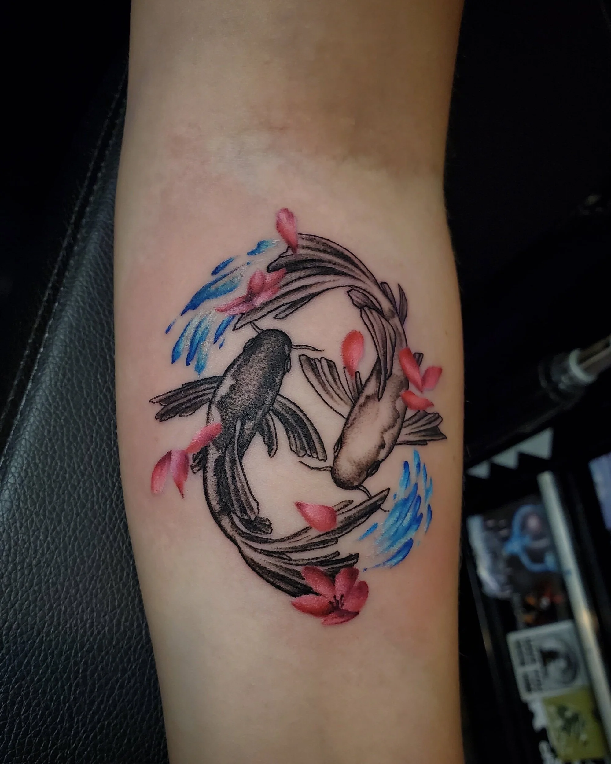 Tattoo of a koi fish with cherry blossoms and water splash details on skin.