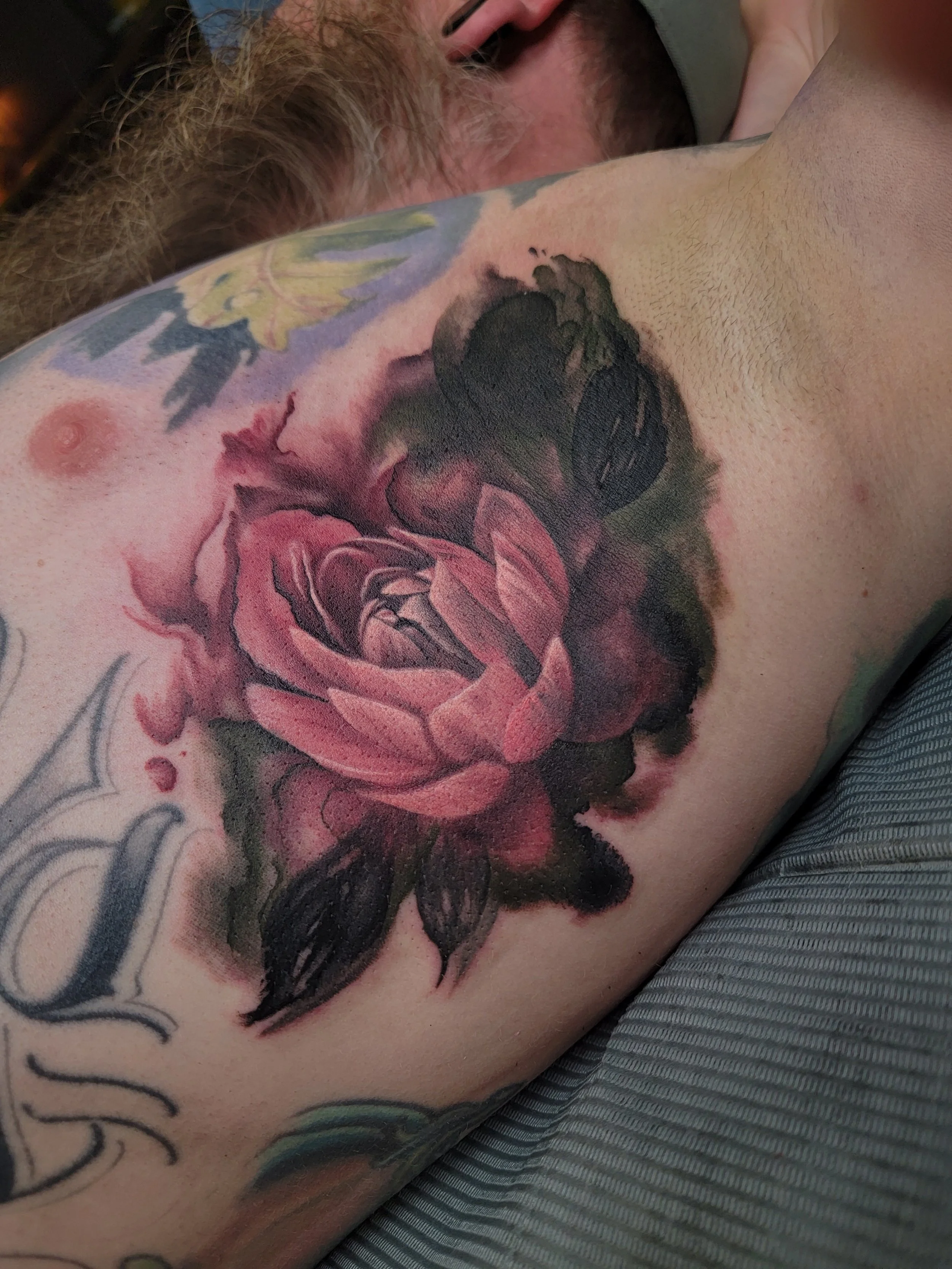 Close-up of a person's rib tattoo of a large pink and black rose with surrounding floral and leaf designs.