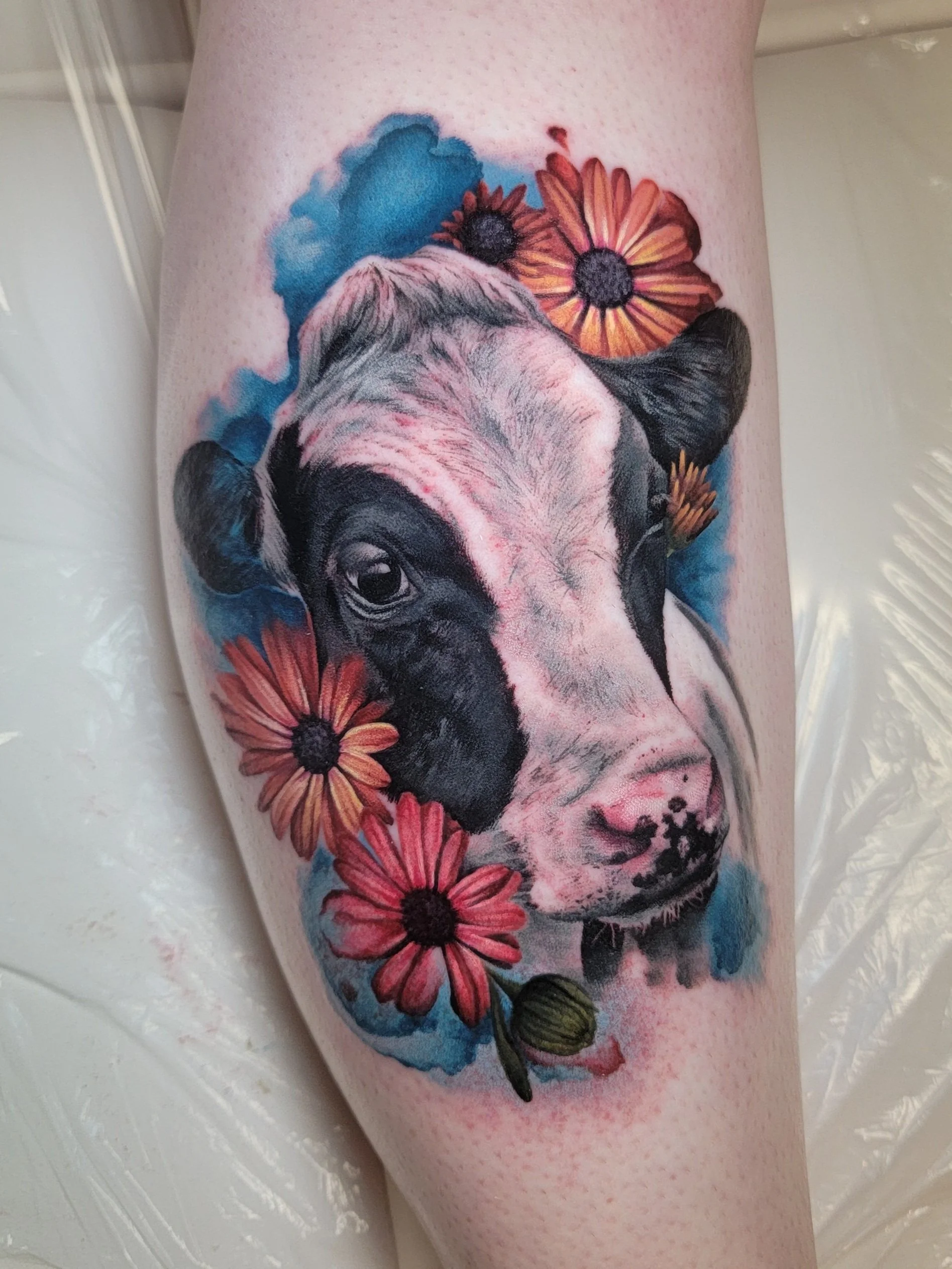 Tattoo of a cow's face with colorful flowers around it on a person's skin.