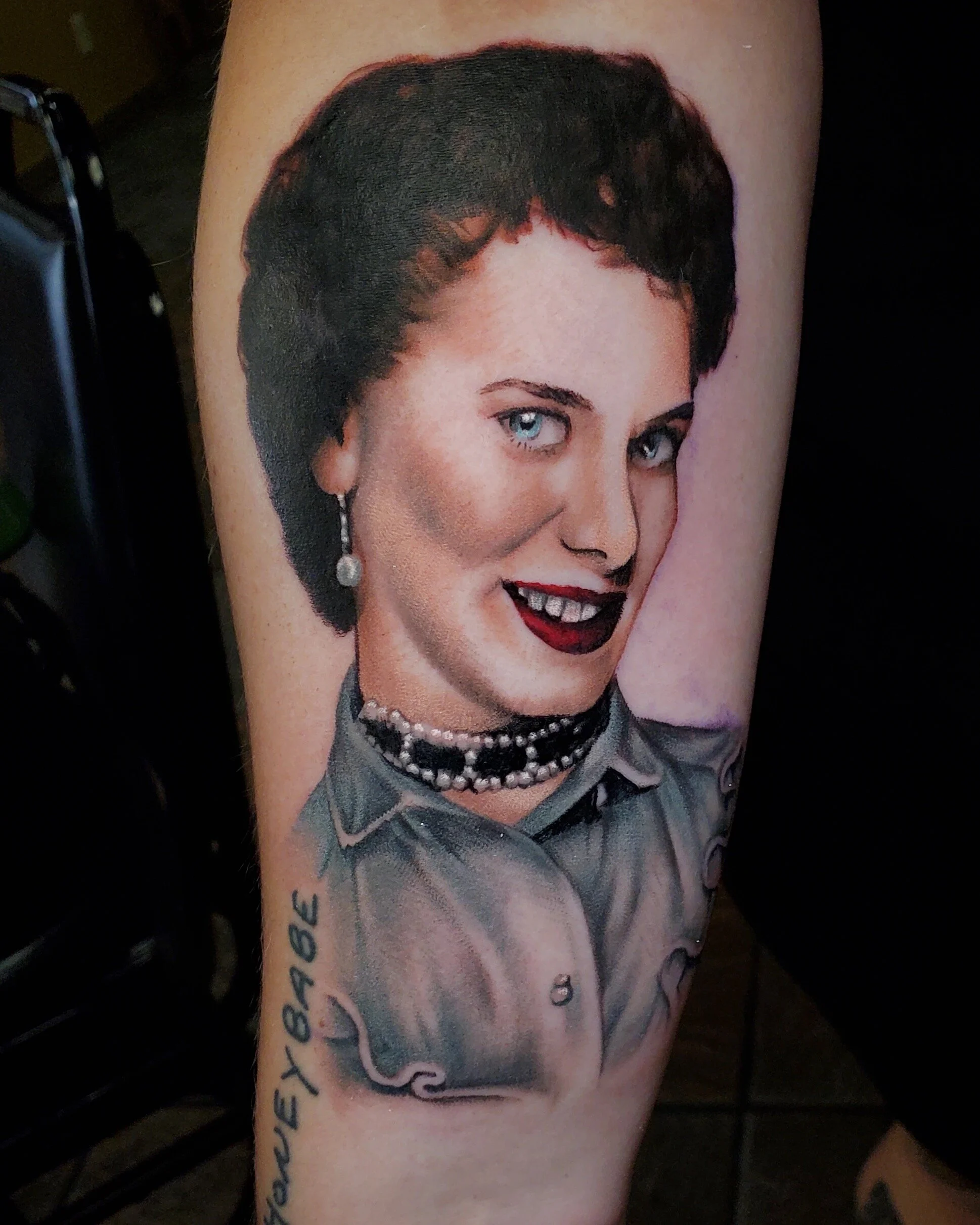 Tattoo of a woman's face with short dark hair, blue eyes, and red lipstick on a person's arm.