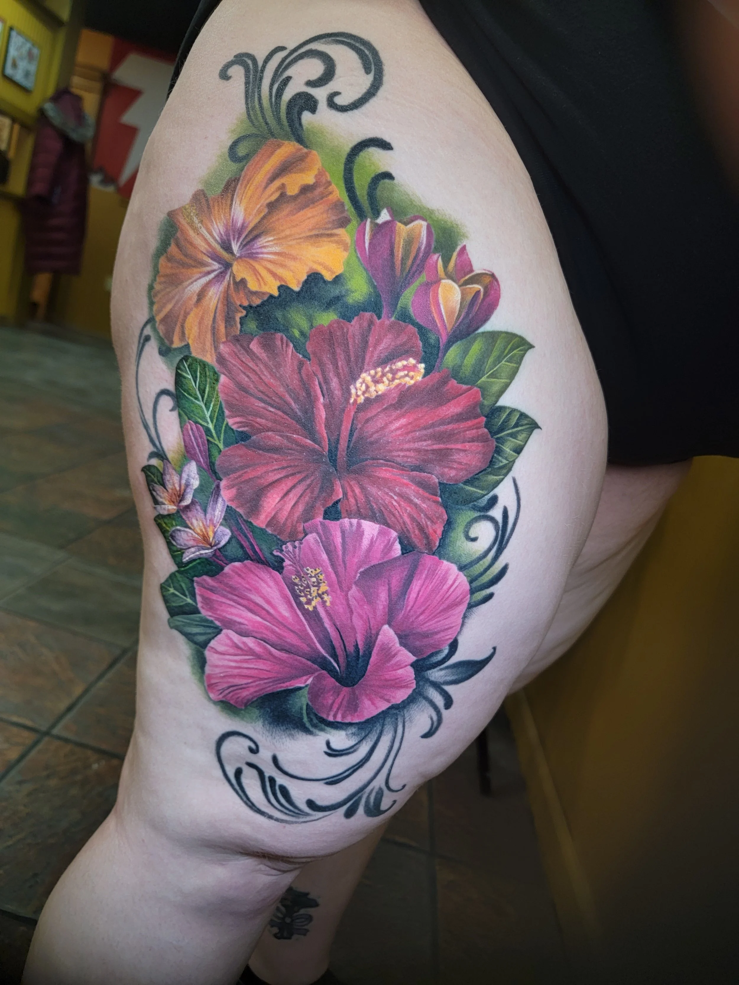 Colorful tattoo of hibiscus flowers and swirling patterns on person's thigh