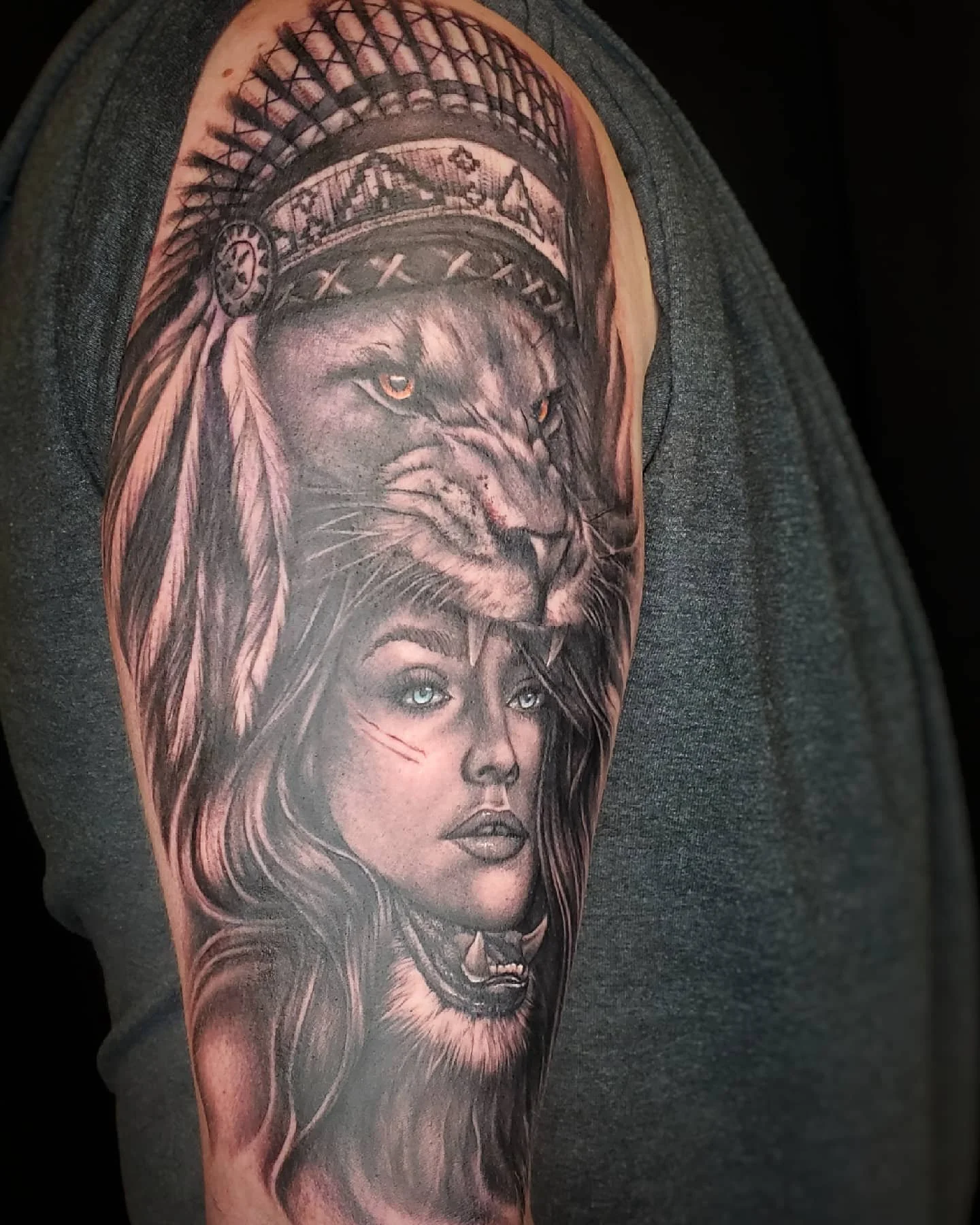 Tattoo of a woman with long hair and a lion with a crown and feathers on her shoulder.