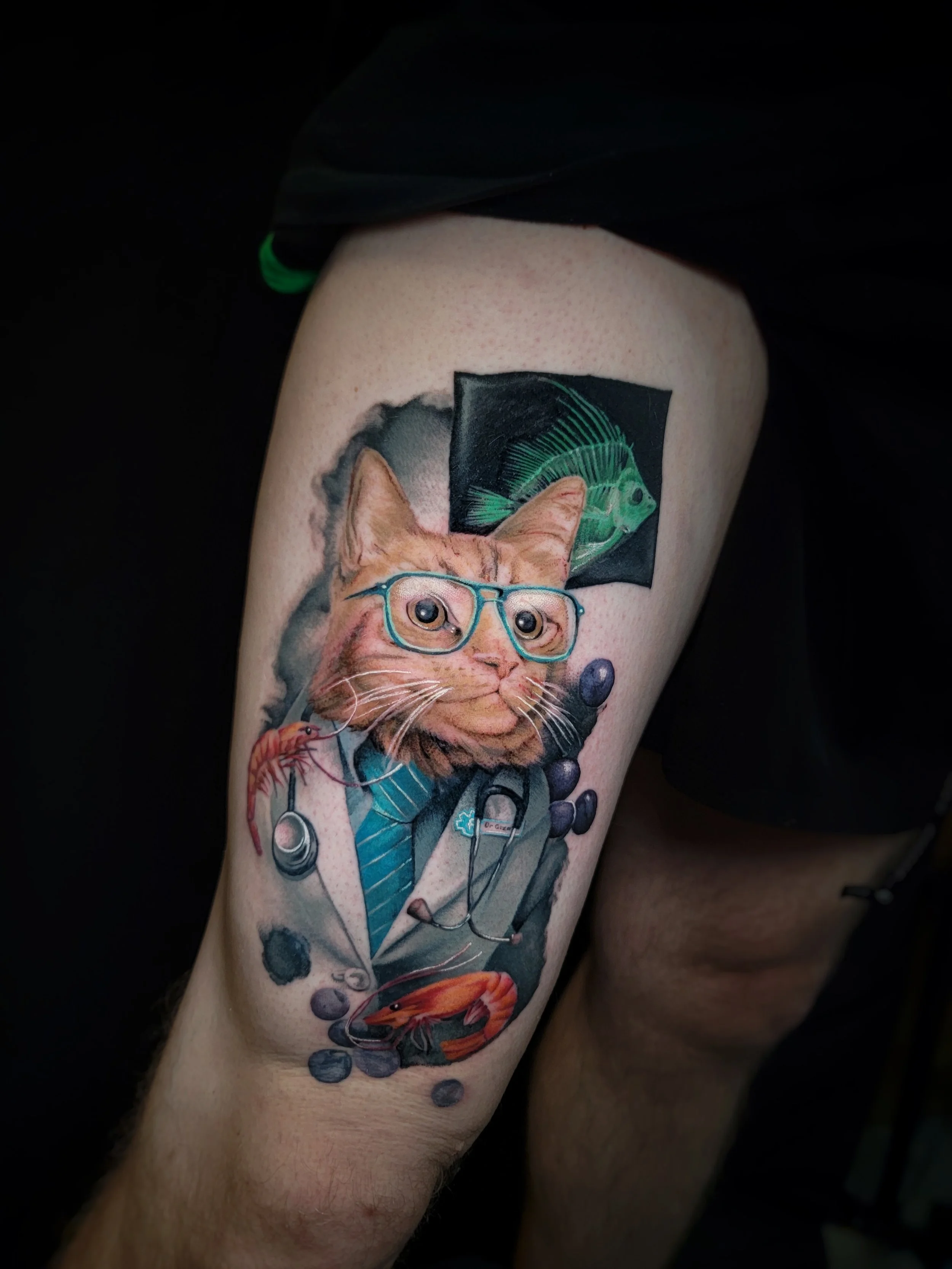 Tattoo of a cat wearing glasses, a stethoscope, and a surgical mask, with a fish in the background.
