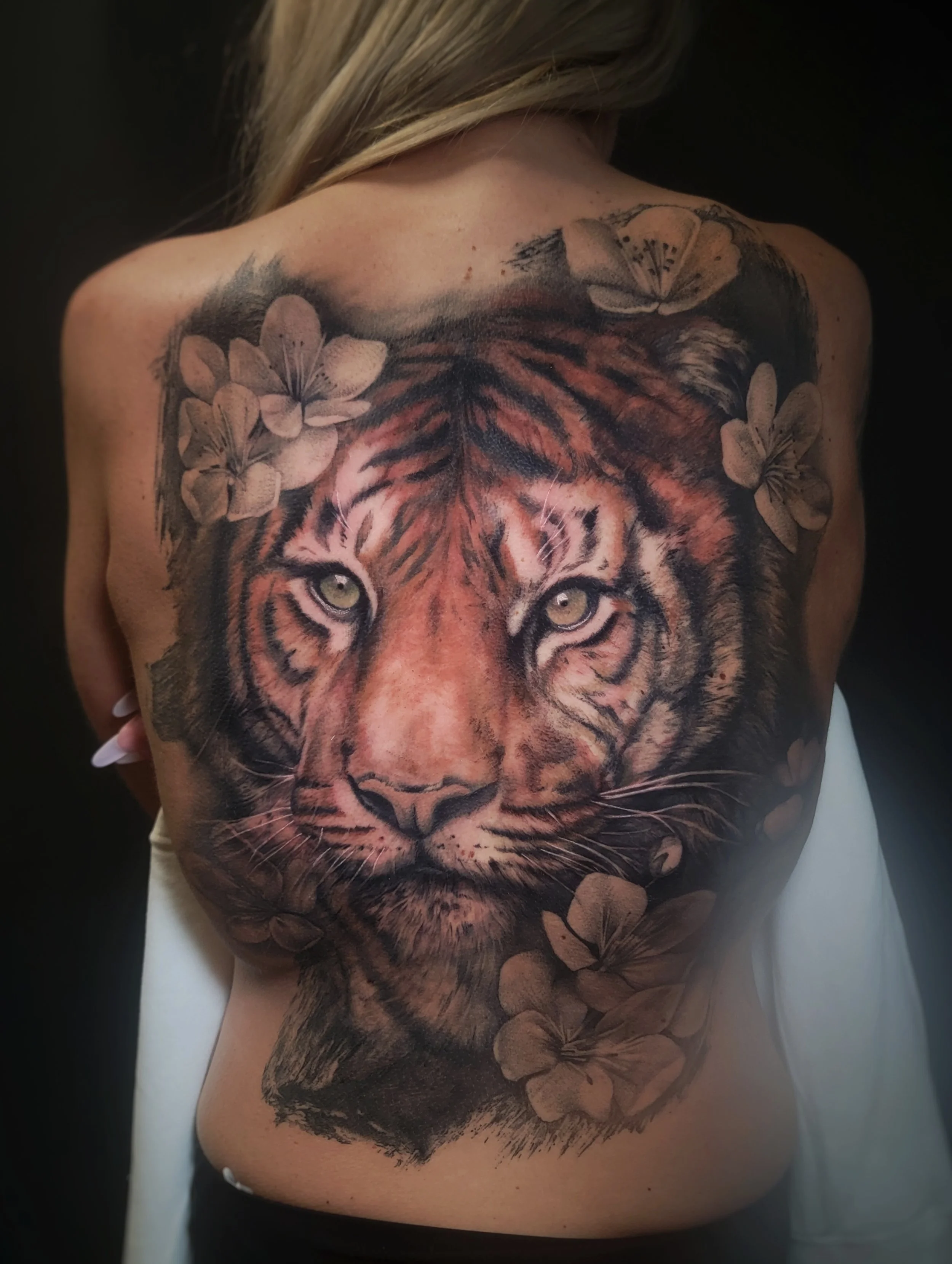 Tattoo of a tiger's face with flowers on a woman's back