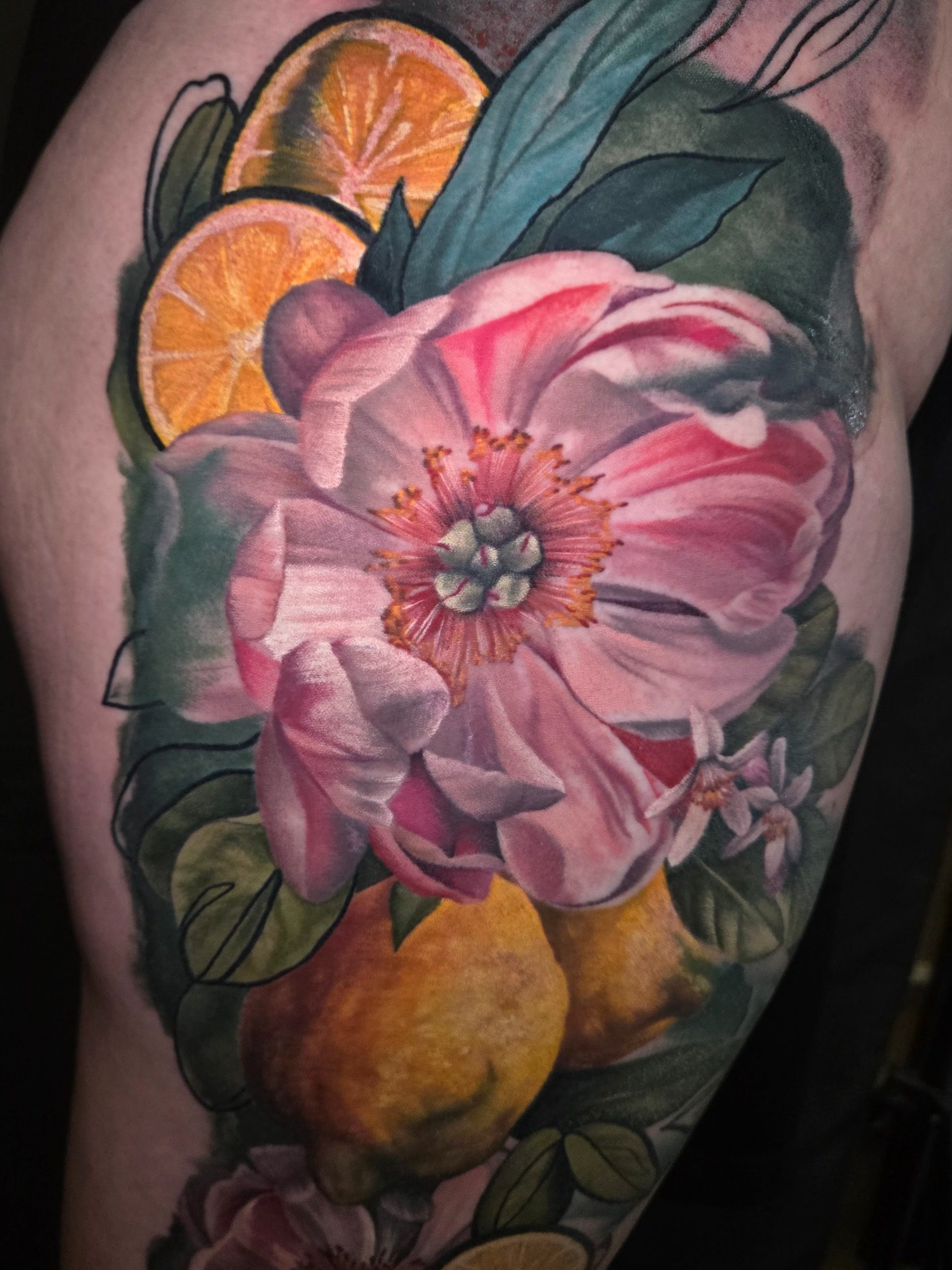 Colorful tattoo of pink flowers, lemon slices, and green leaves.