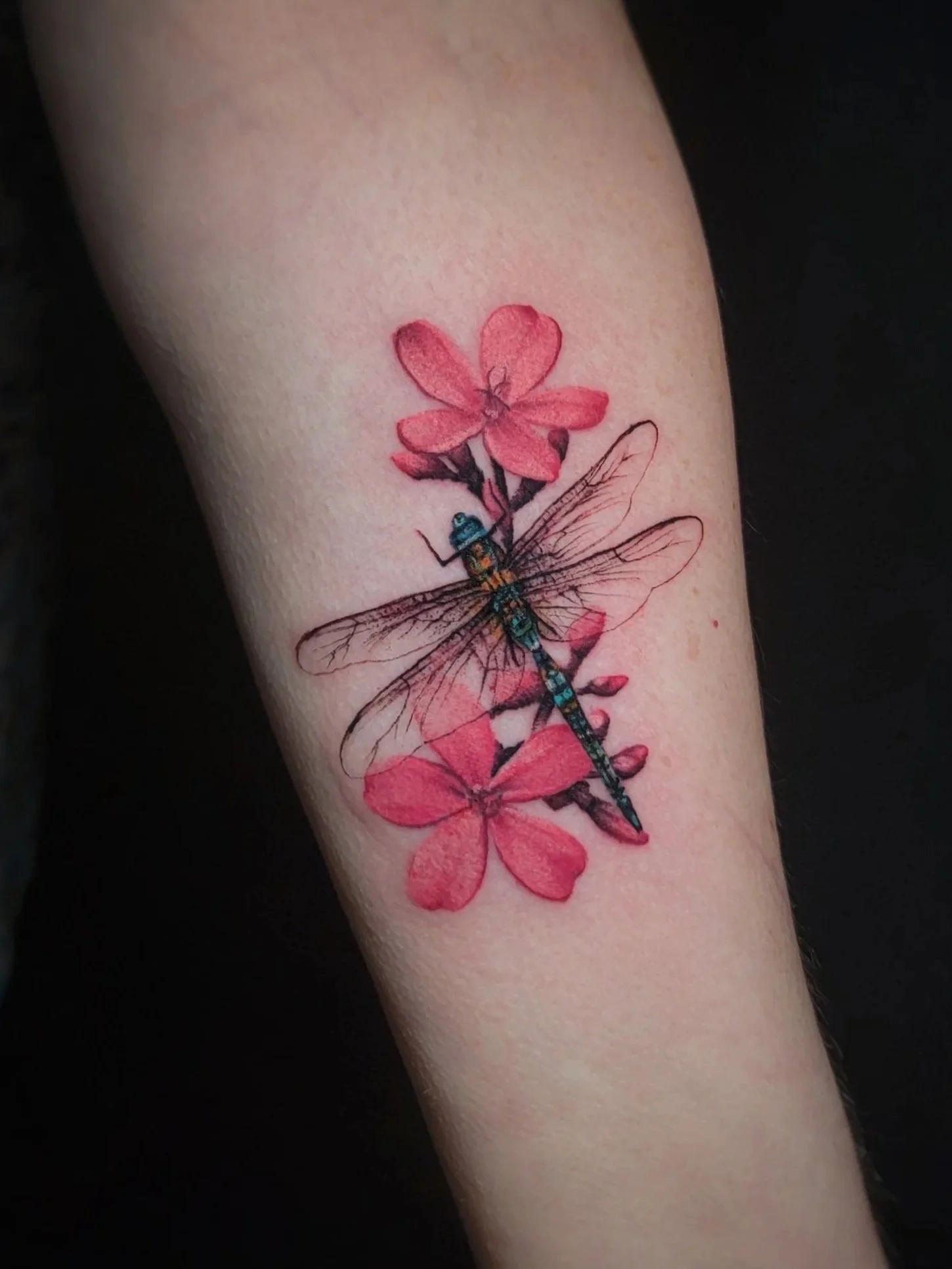 Tattoo of a pink flower with a dragonfly on a person's skin.