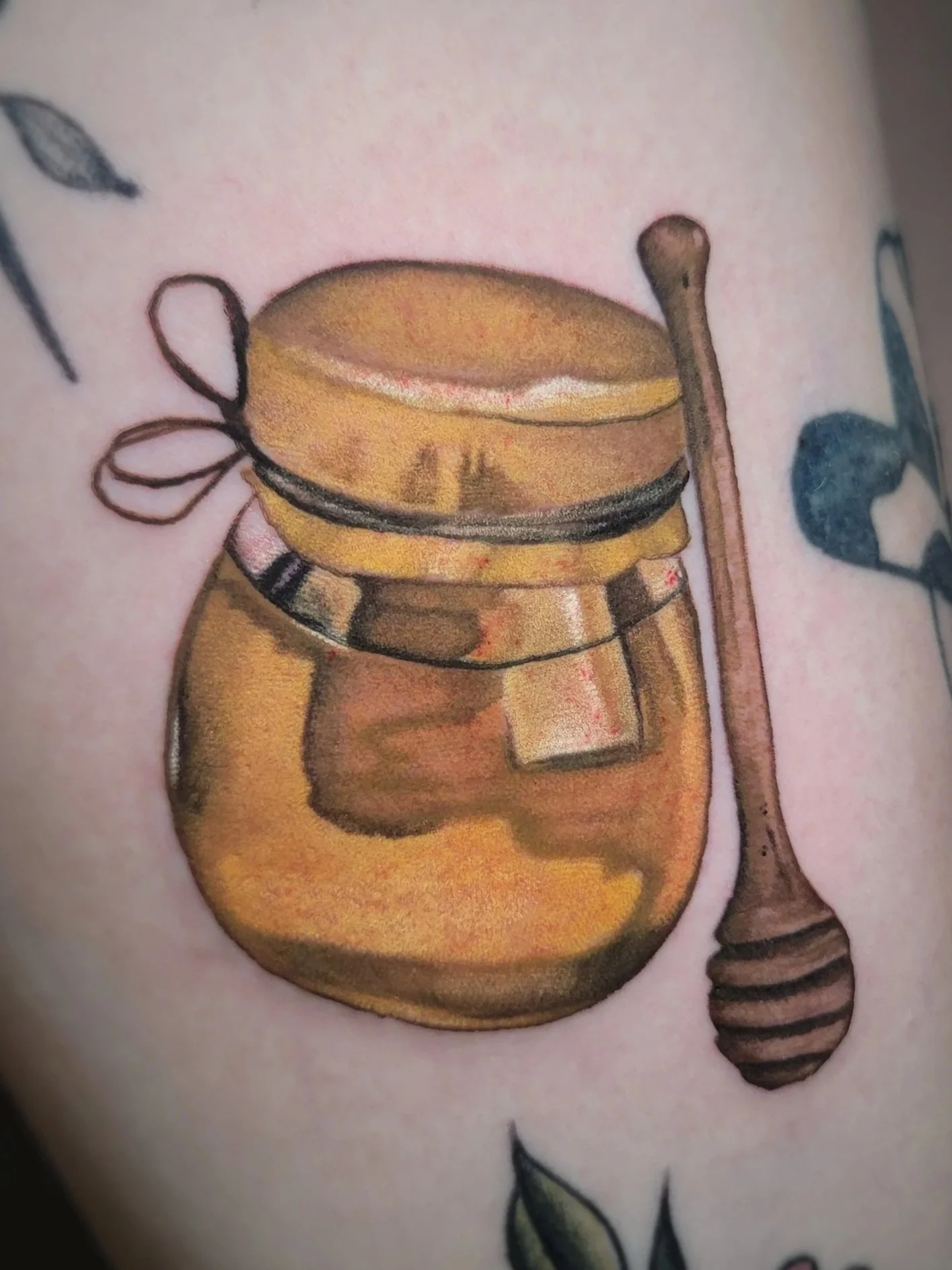 A tattoo of a honey jar with a honey dipper on skin.
