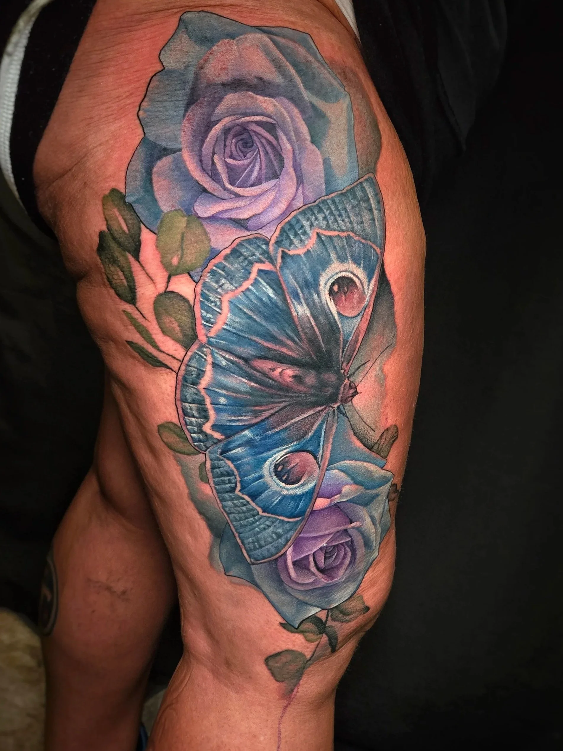 Tattoo of purple roses and blue moth on a person's thigh.