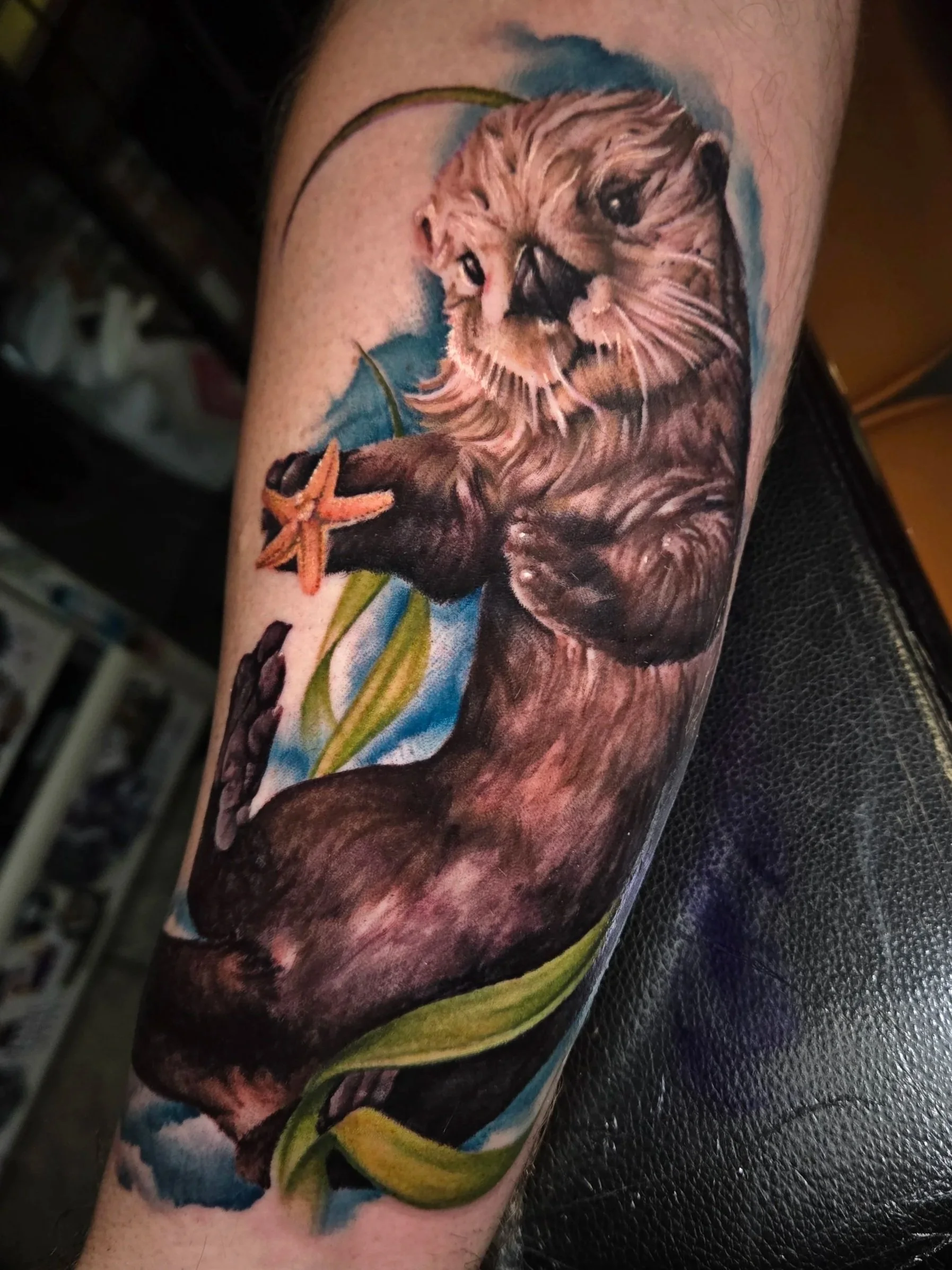 Colorful arm tattoo of an otter with a starfish and marine-themed background.