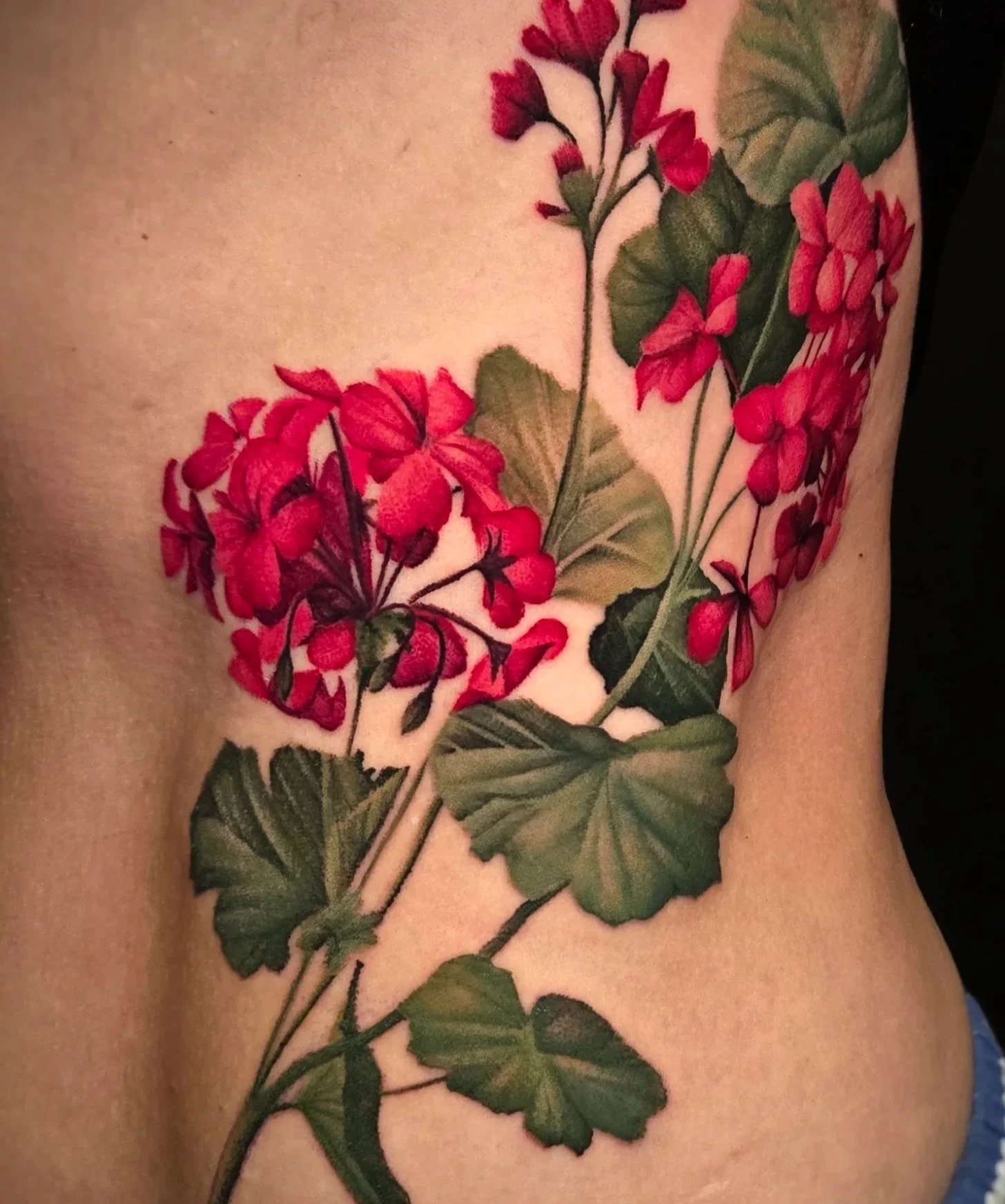 Close-up of a tattoo featuring red and pink flowers with green leaves on a person's skin.
