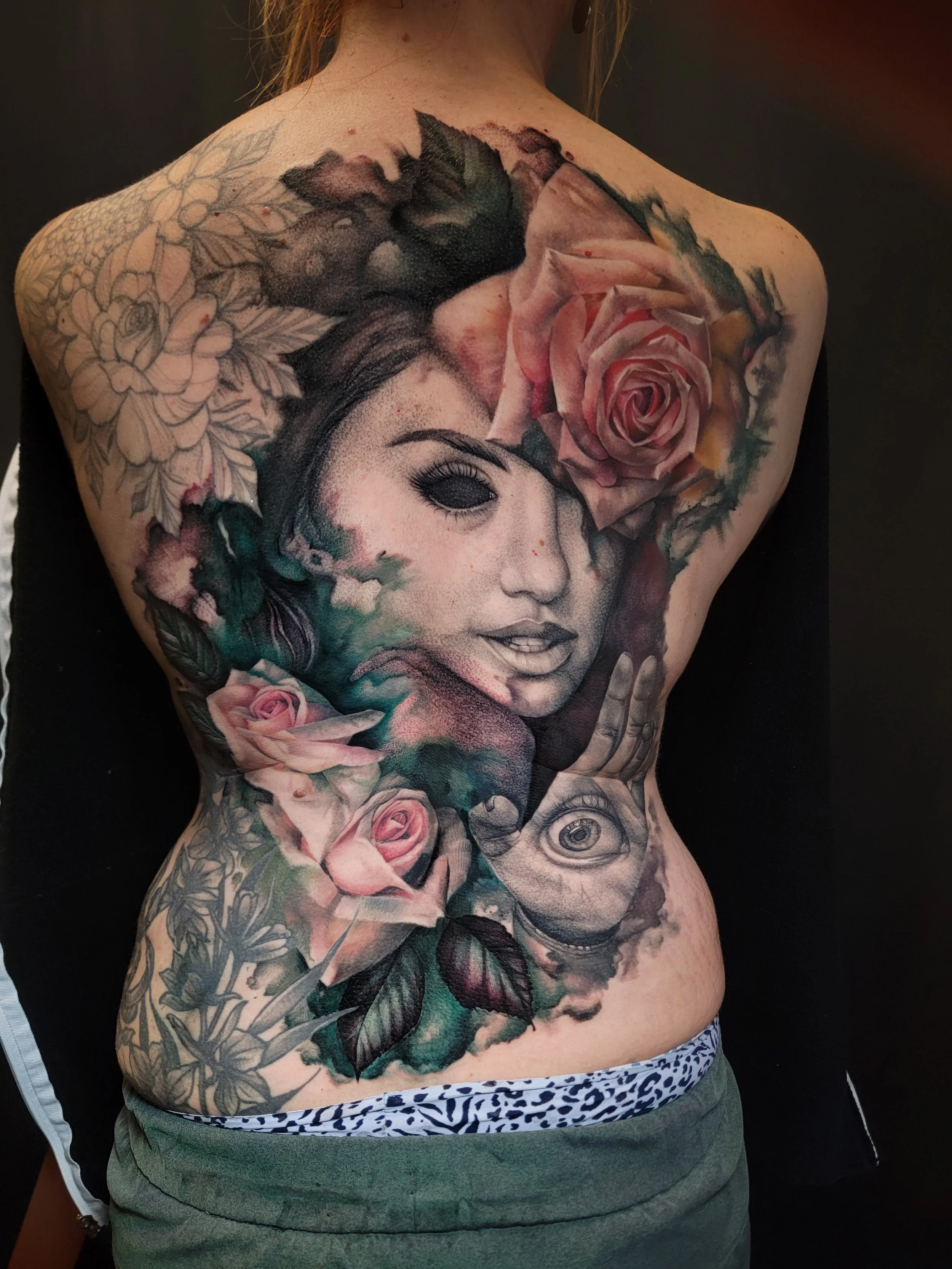 A person's back with a large tattoo of a woman's face surrounded by rose and leaves