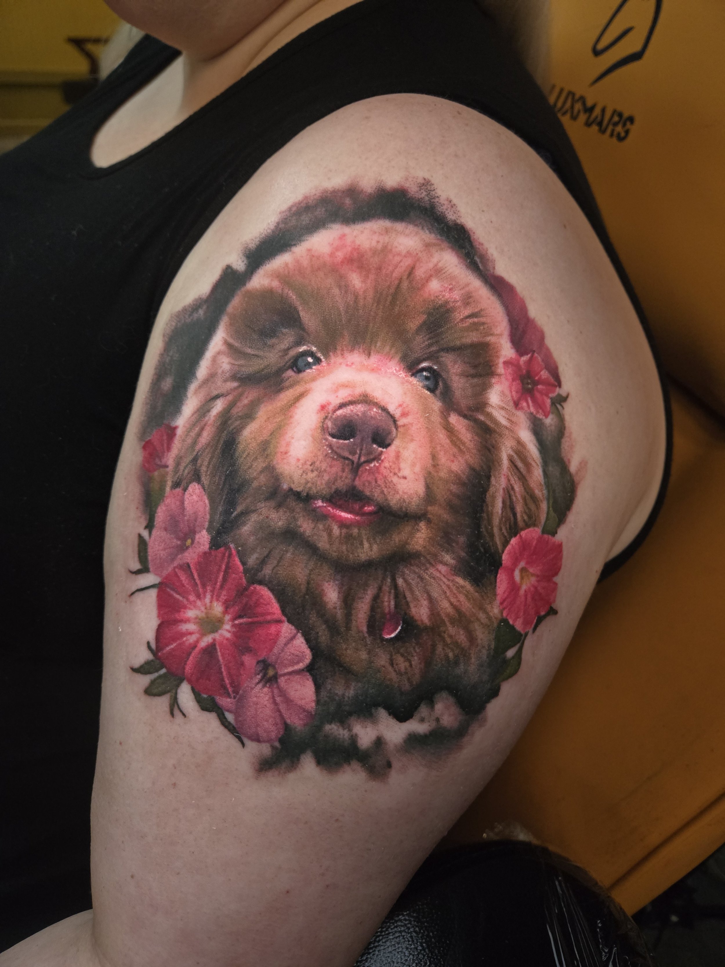 Tattoo of a puppy surrounded by pink flowers on a person's upper arm.