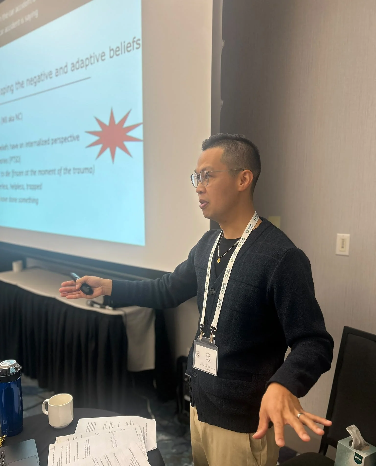 Kyle Poon teaching about negative and positive beliefs in EMDR beside a projected slide