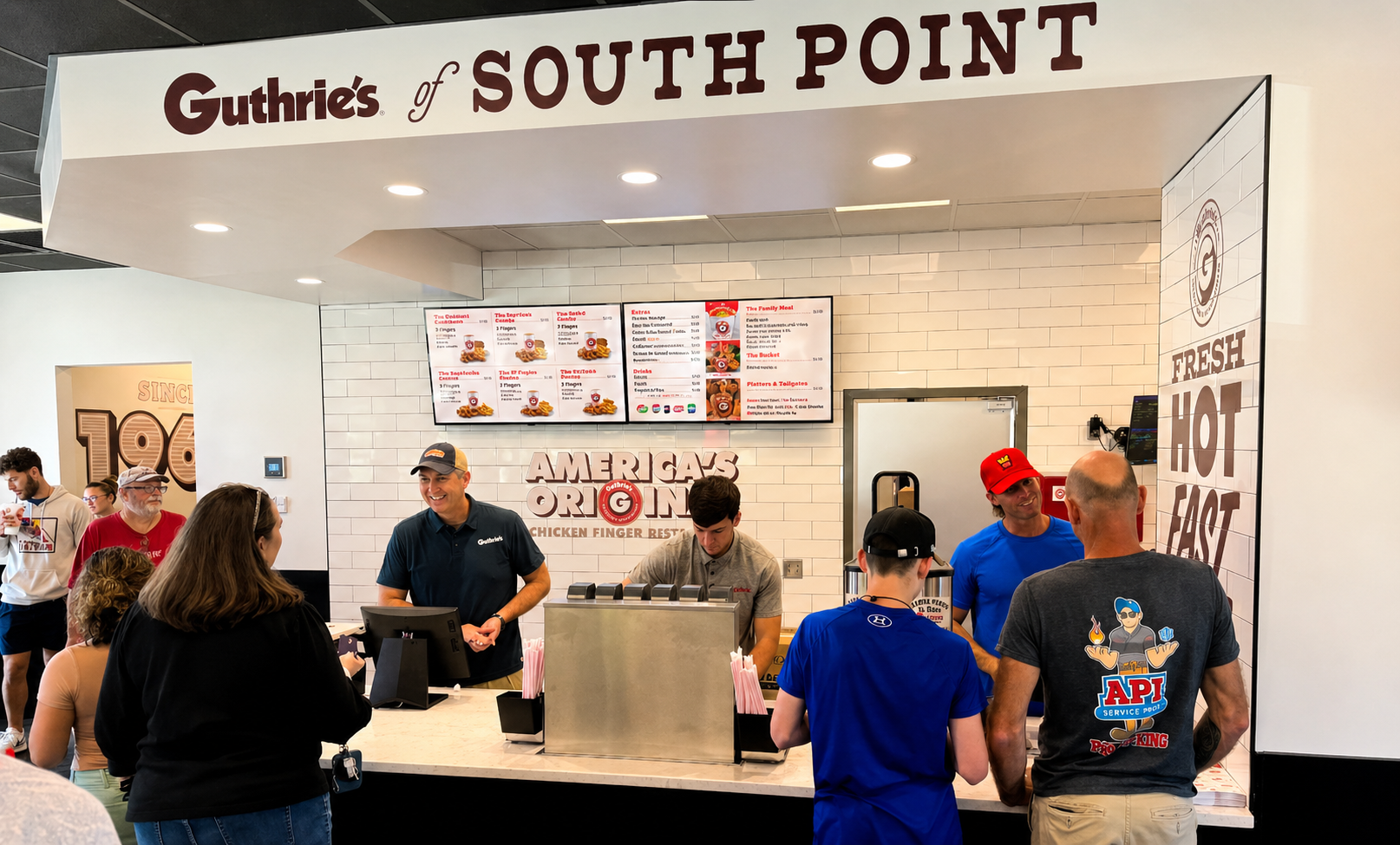 Guthrie's of South Point counter with customers and staff, menu on digital screens, white brick wall background, promotional signage, people ordering and chatting.