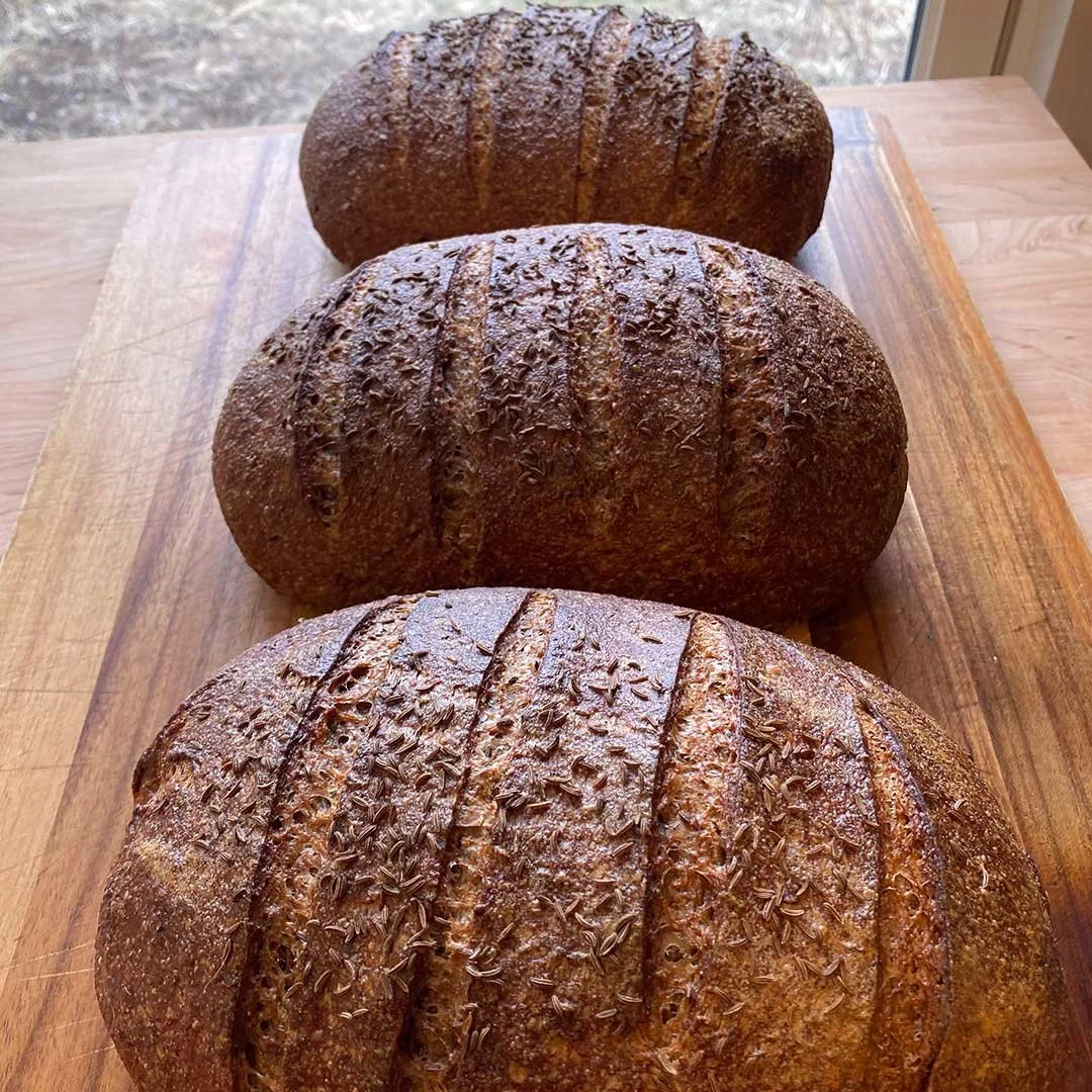 Three loves of rye bread sitting on a cutting board.