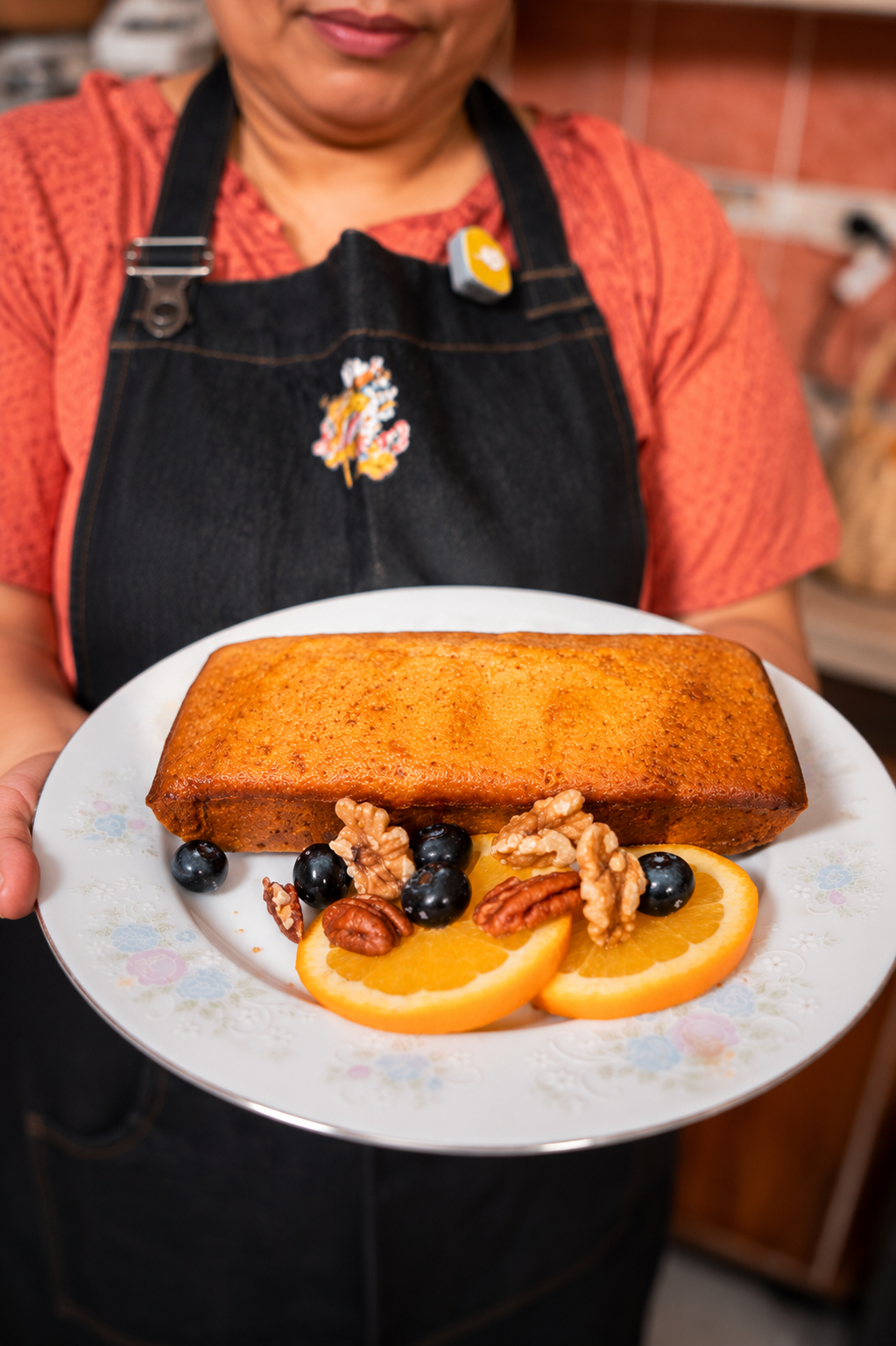 Persona sosteniendo un plato con un pastel de manzana, rodajas de naranja, nueces y uvas.