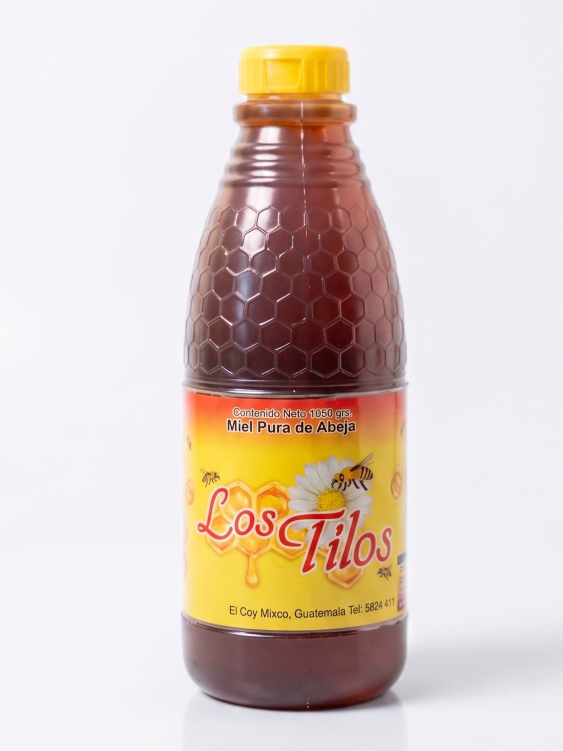 Botella de miel pura de abeja con etiqueta amarilla y detalles en naranja, con flores y abejas ilustradas, y texto en español, en una superficie blanca.