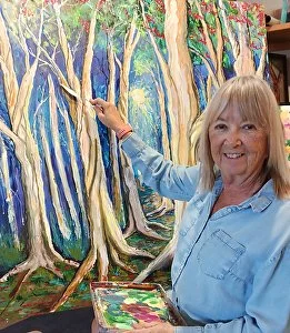 Woman painting a forest scene with tall trees and green foliage
