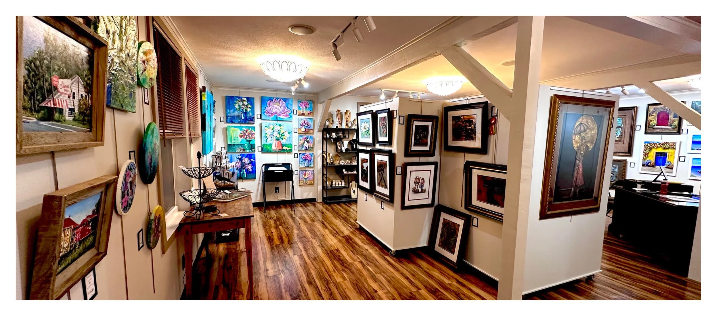 An art gallery showcasing colorful paintings and framed artwork on white walls with hardwood flooring and track lighting.