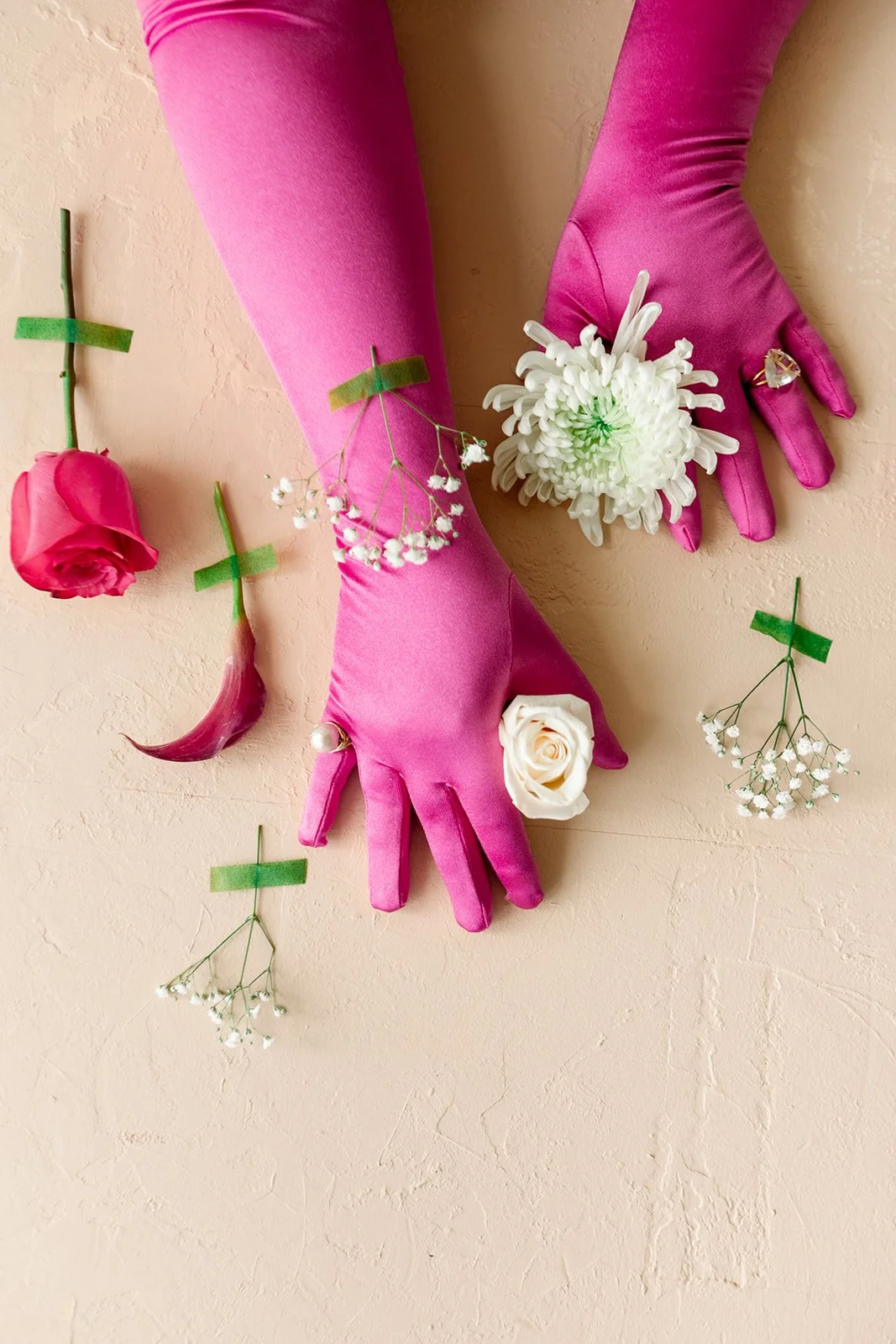 Two hands in bright pink gloves holding white flowers against a beige wall, with pink and white flowers and a pink horn on the wall.