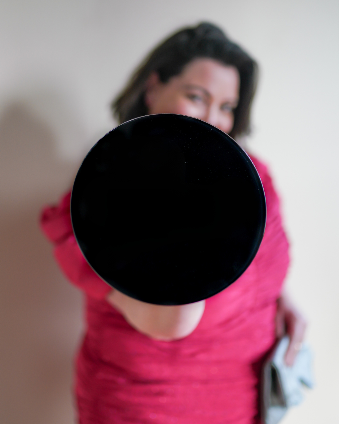 Summer Carrick is a top social media marketing expert, wearing pink top holding a black circular object towards the camera, face blurry in the background.