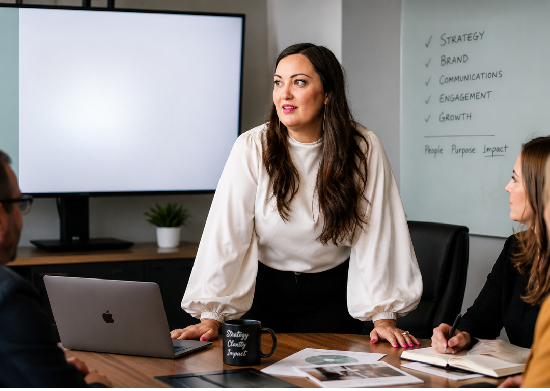 Summer Carrick standing at a conference table with a laptop, whiteboard, with marketing clients during a Portland, Oregon consult.