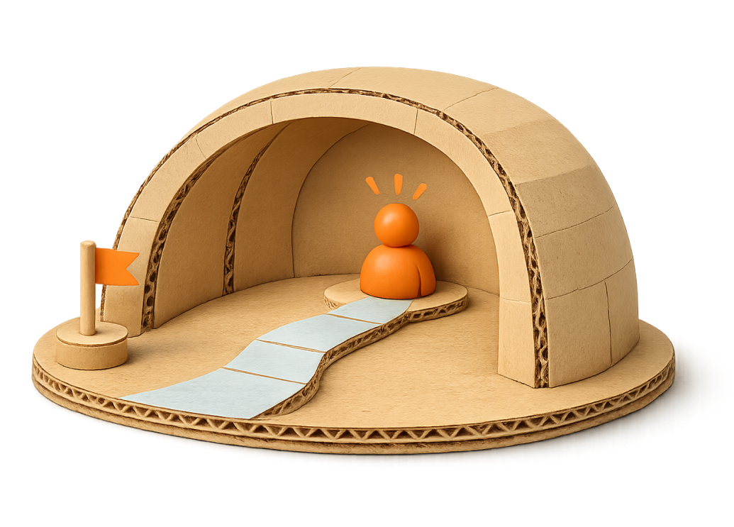 A cardboard nativity scene with a small pathway leading to an orange figure inside a stable, featuring a flag on one side.