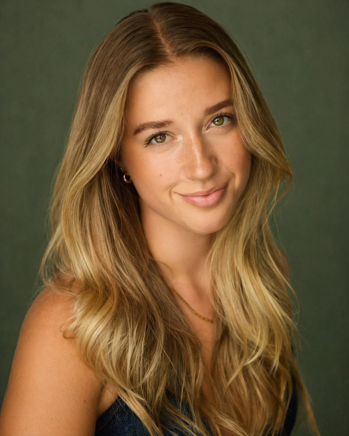A young woman with long, wavy blonde hair and light green eyes smiling softly at the camera with a green background.