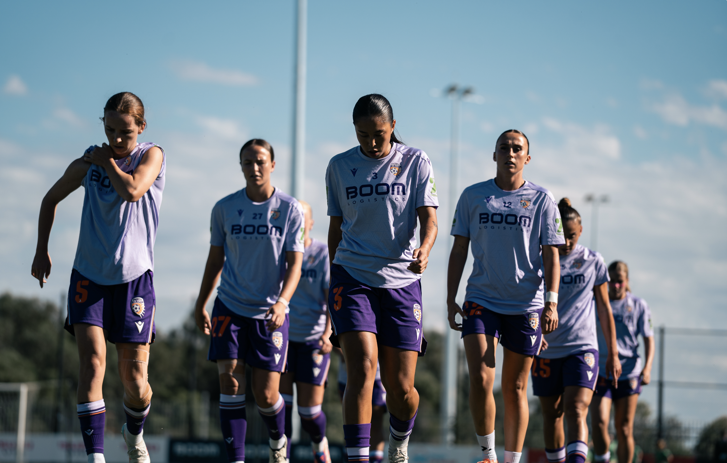 Women soccer players in white and purple uniforms walking on a soccer field.