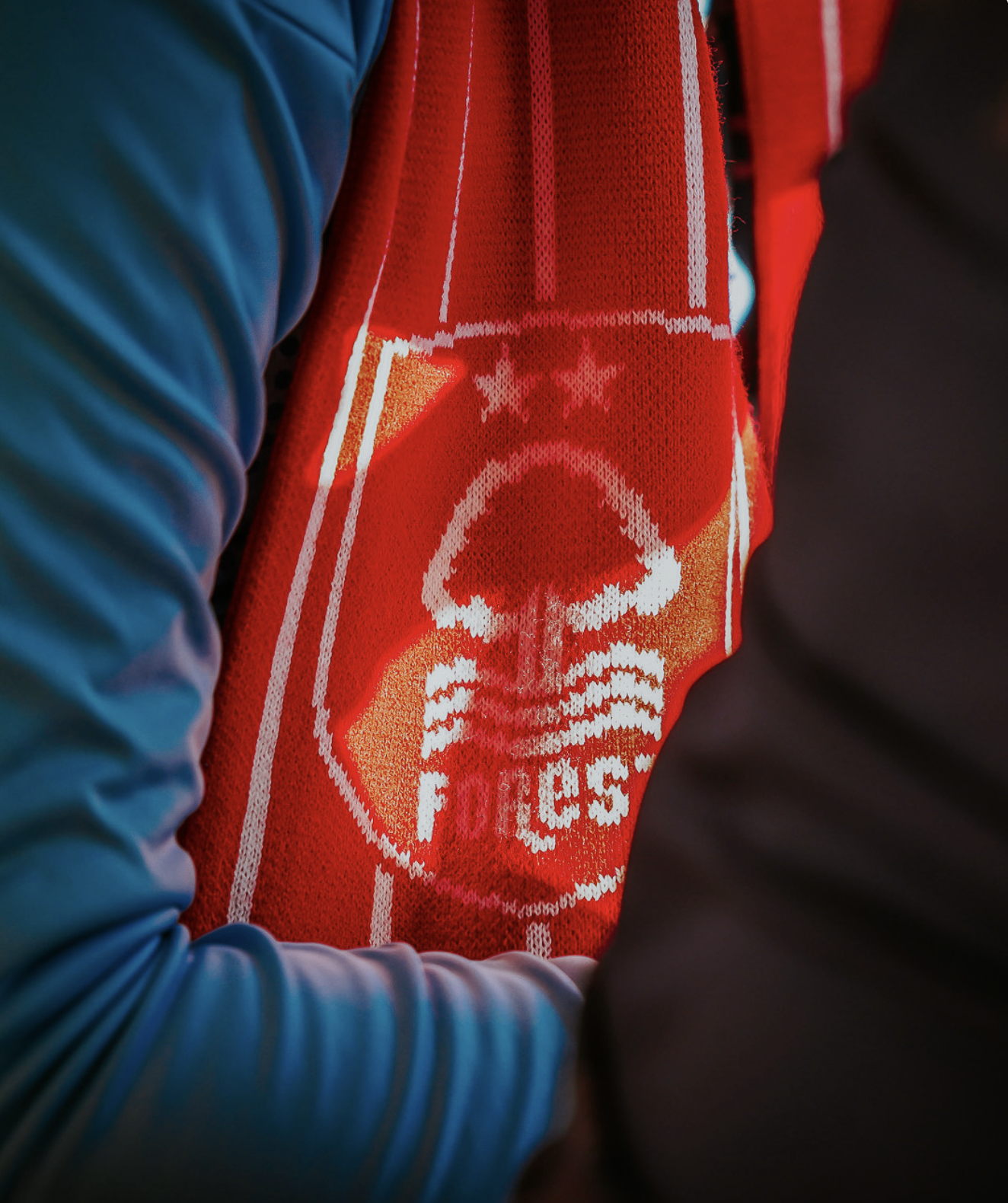 Close-up of a person wearing a red scarf with a Skull Vikings logo and the words 'F.C. 55' on it, with a blue jacket on their arm.