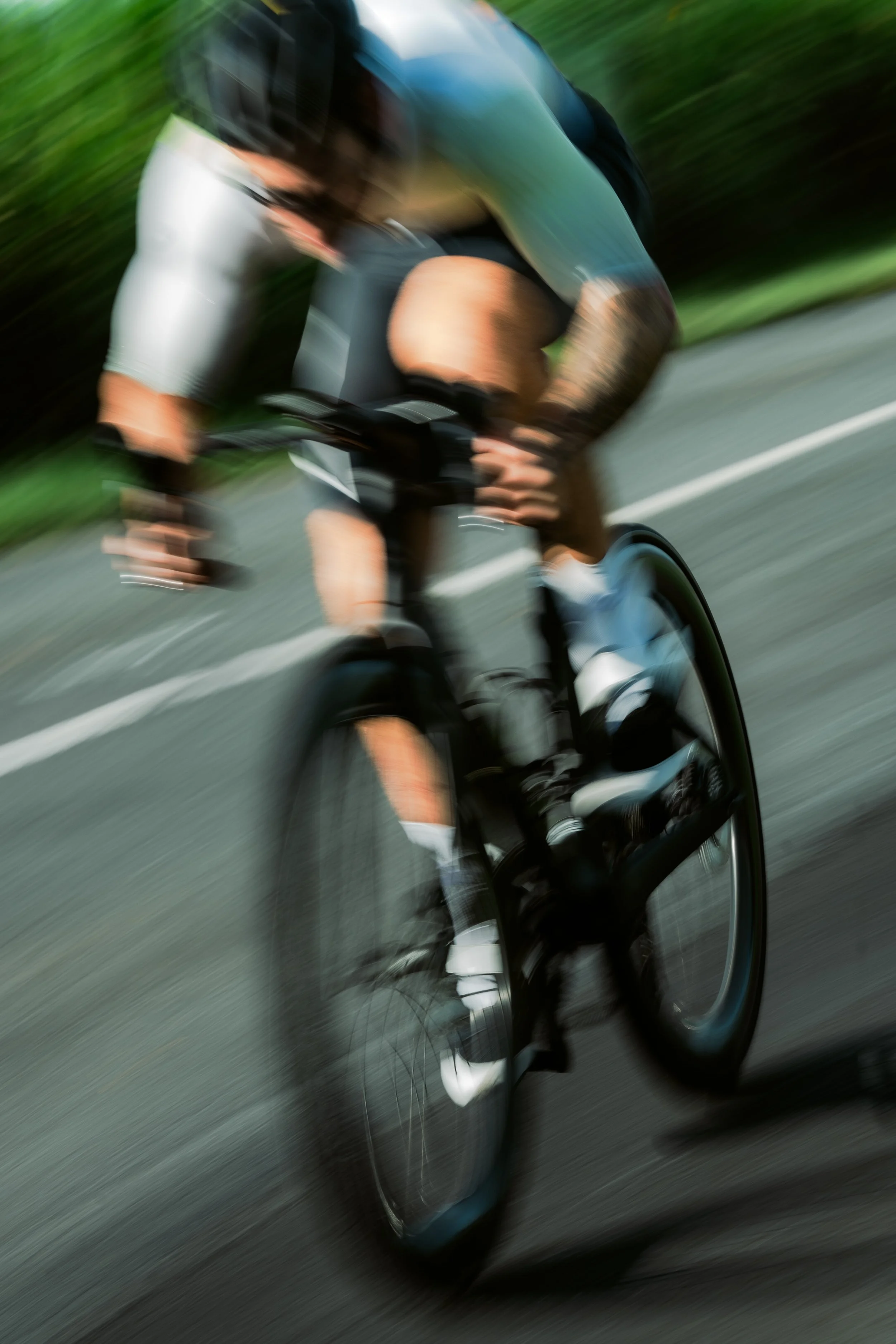 A blurred image of a cyclist riding a bike on a road with green trees in the background.