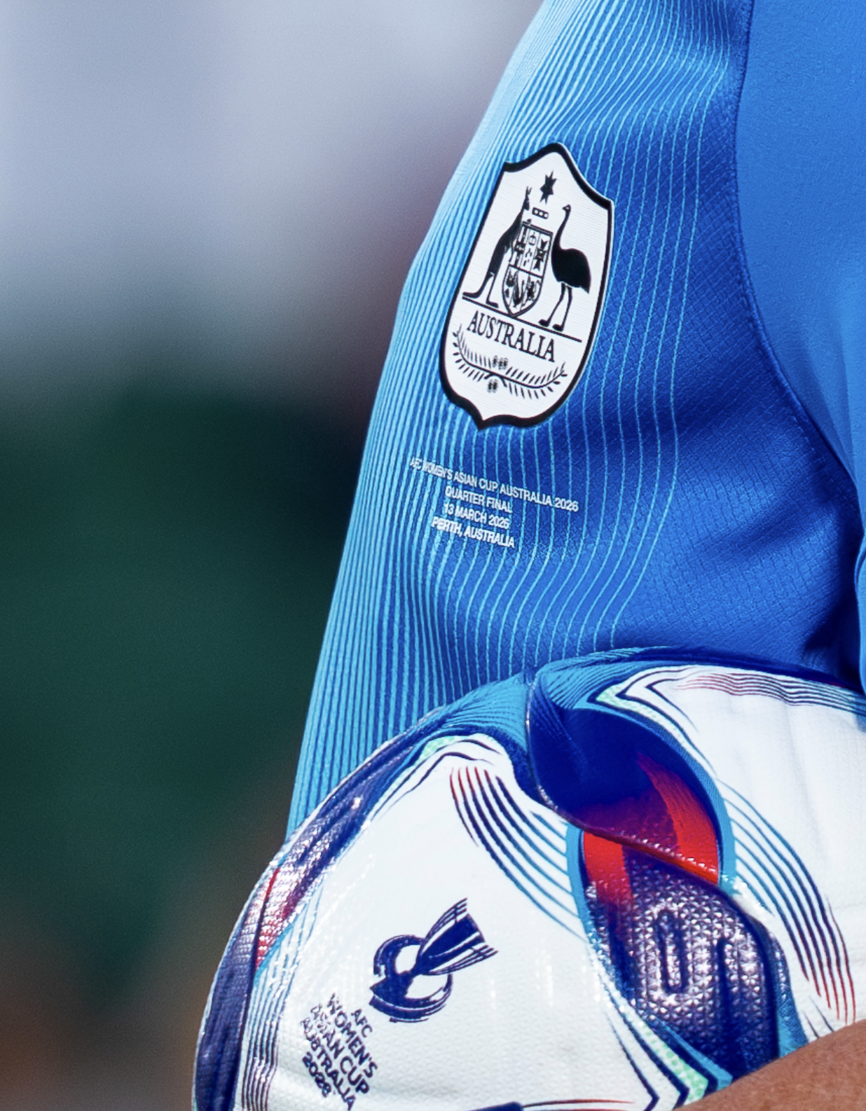 Close-up of a sports uniform with a badge of the Australian coat of arms and text indicating it is for the AFC Asian Cup Australia 2026 quarter-final, held in Perth, Australia on March 13, 2026.
