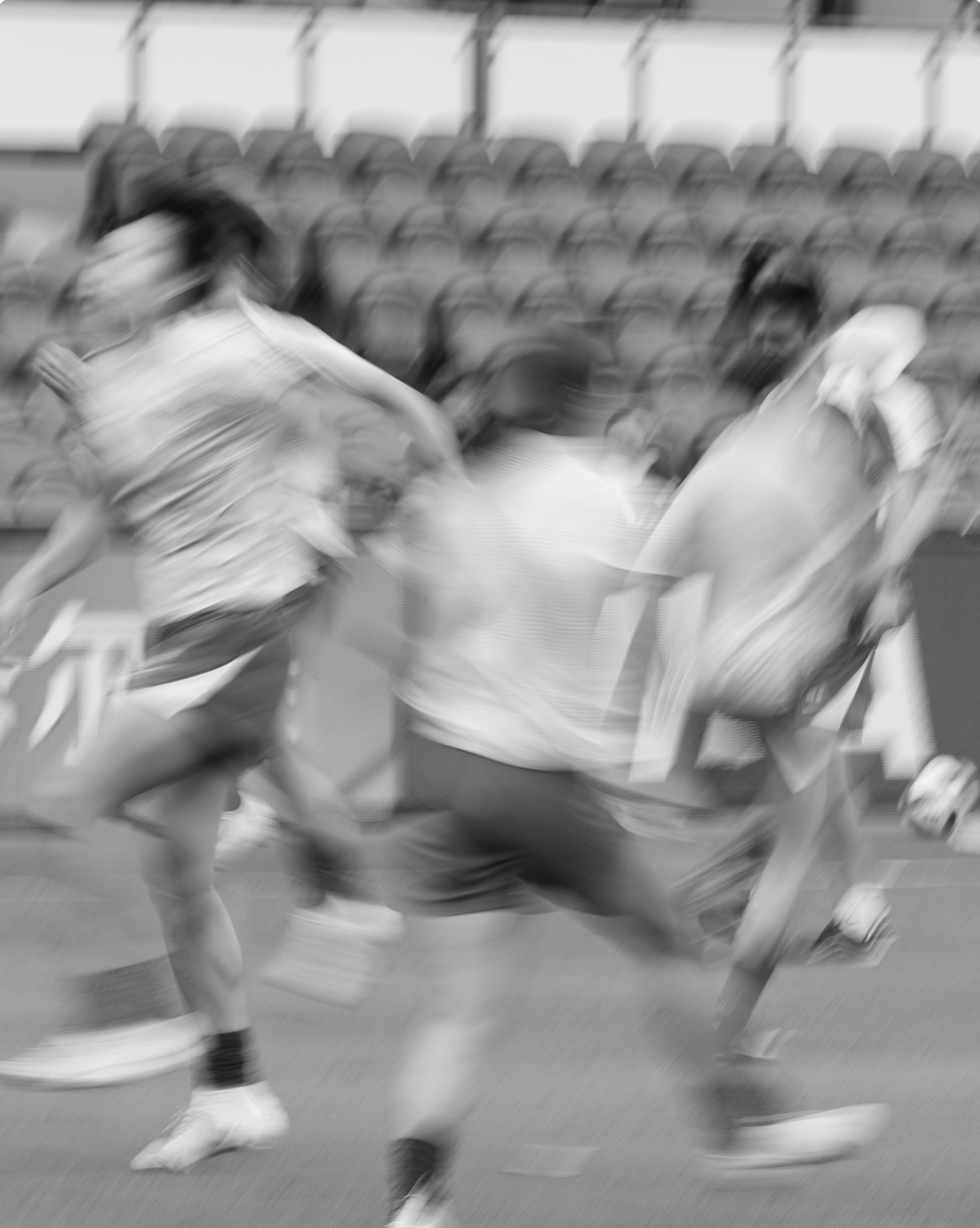 Blurry black-and-white photo of people running on a track at an athletics stadium.