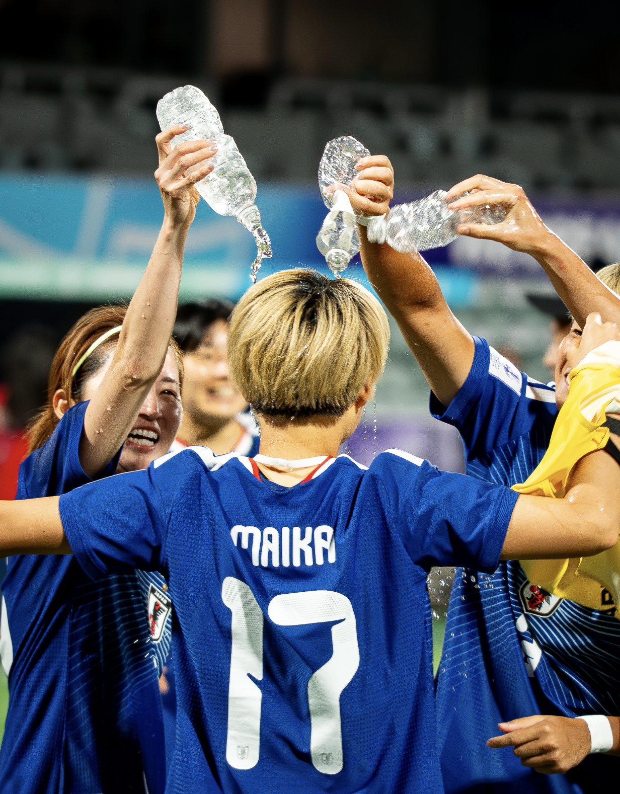 Soccer players celebrating with water bottles, wearing blue jerseys, in a stadium.