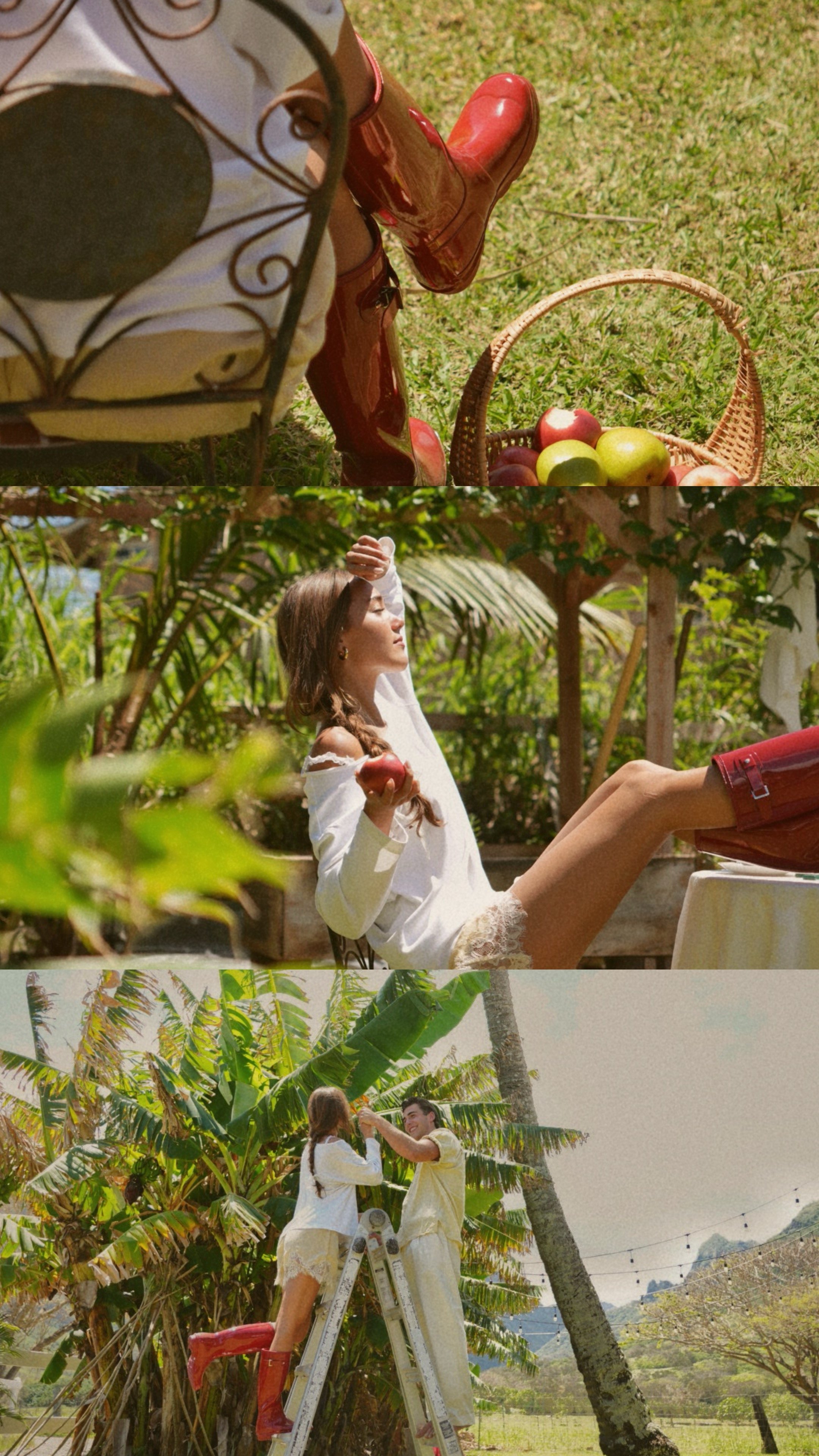 A woman with long brown hair sitting on a table outdoors in the sun, holding an apple in her right hand, surrounded by lush green trees and foliage, wearing a white dress with lace at the bottom, and red rain boots.