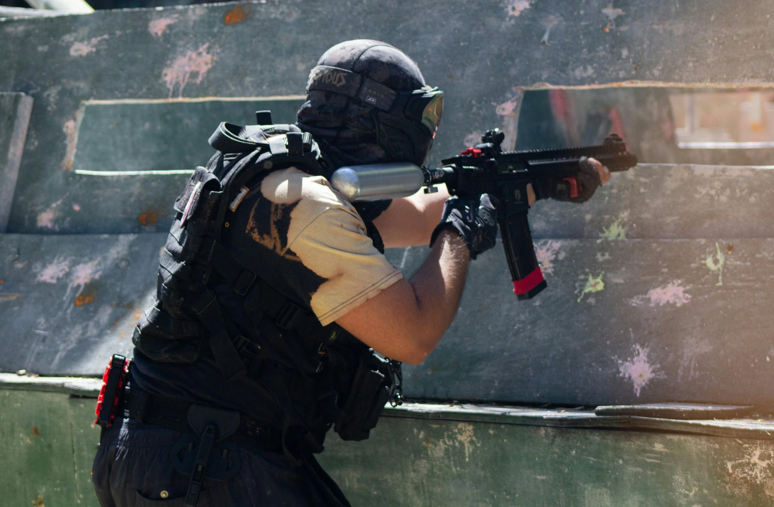 A person wearing tactical gear, including a helmet and gloves, aiming an airsoft gun through a shooting range barrier in central alberta.