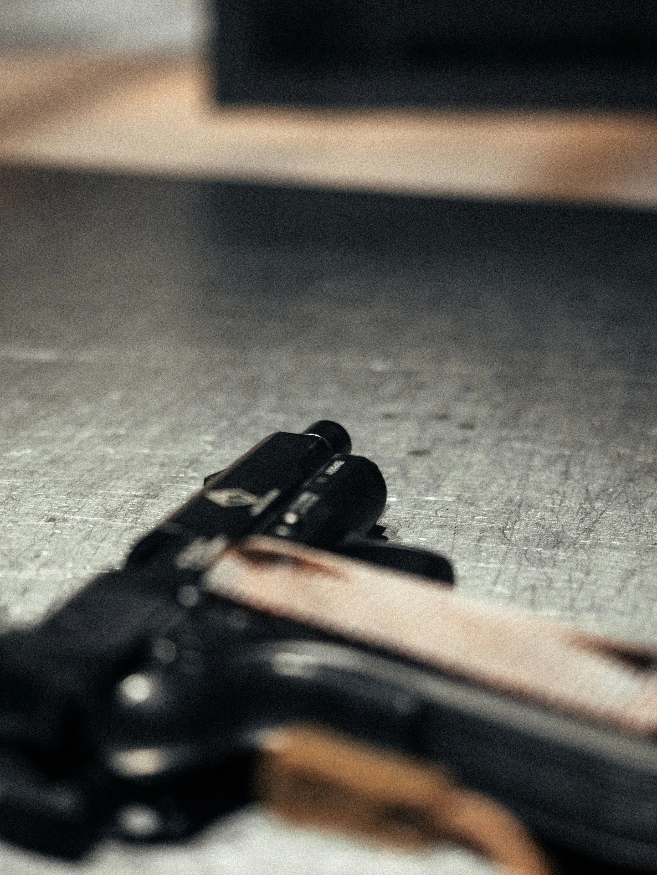 Close-up of a firearm on a gray textured surface, viewed from below with a blurred background for gun range in central alberta.