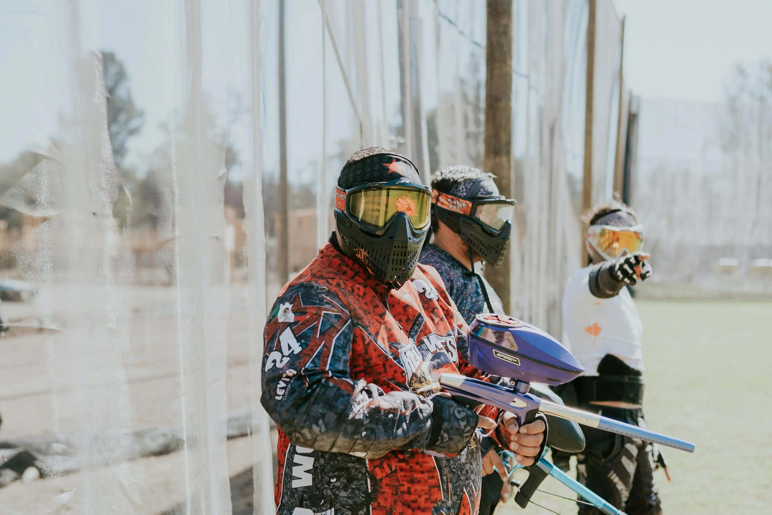 Two people wearing motocross gear and paintball masks, standing in an outdoor paintball arena in central alberta.