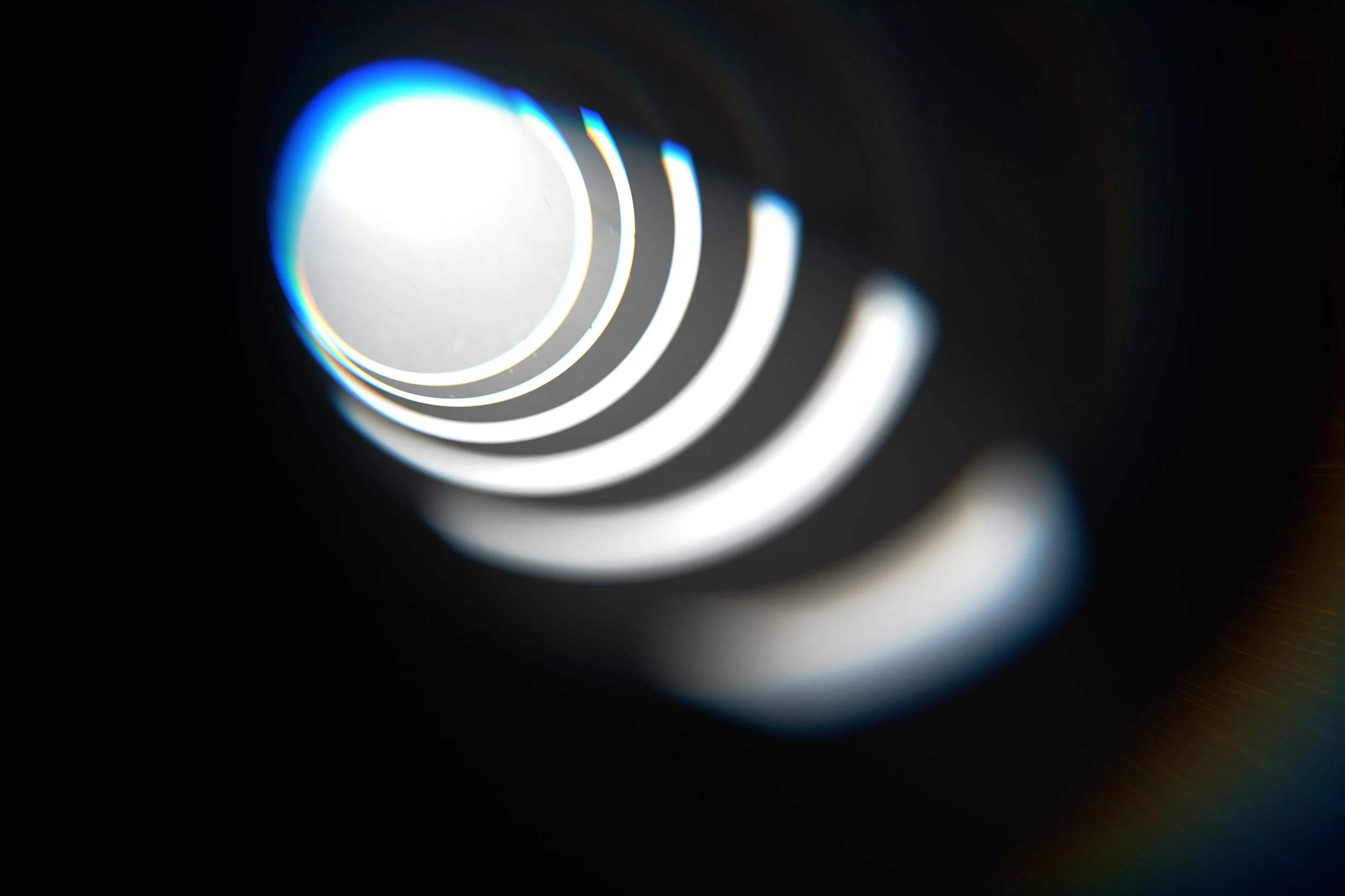 Close-up of a circular object emitting bright white light with rainbow-colored reflection on a black background.