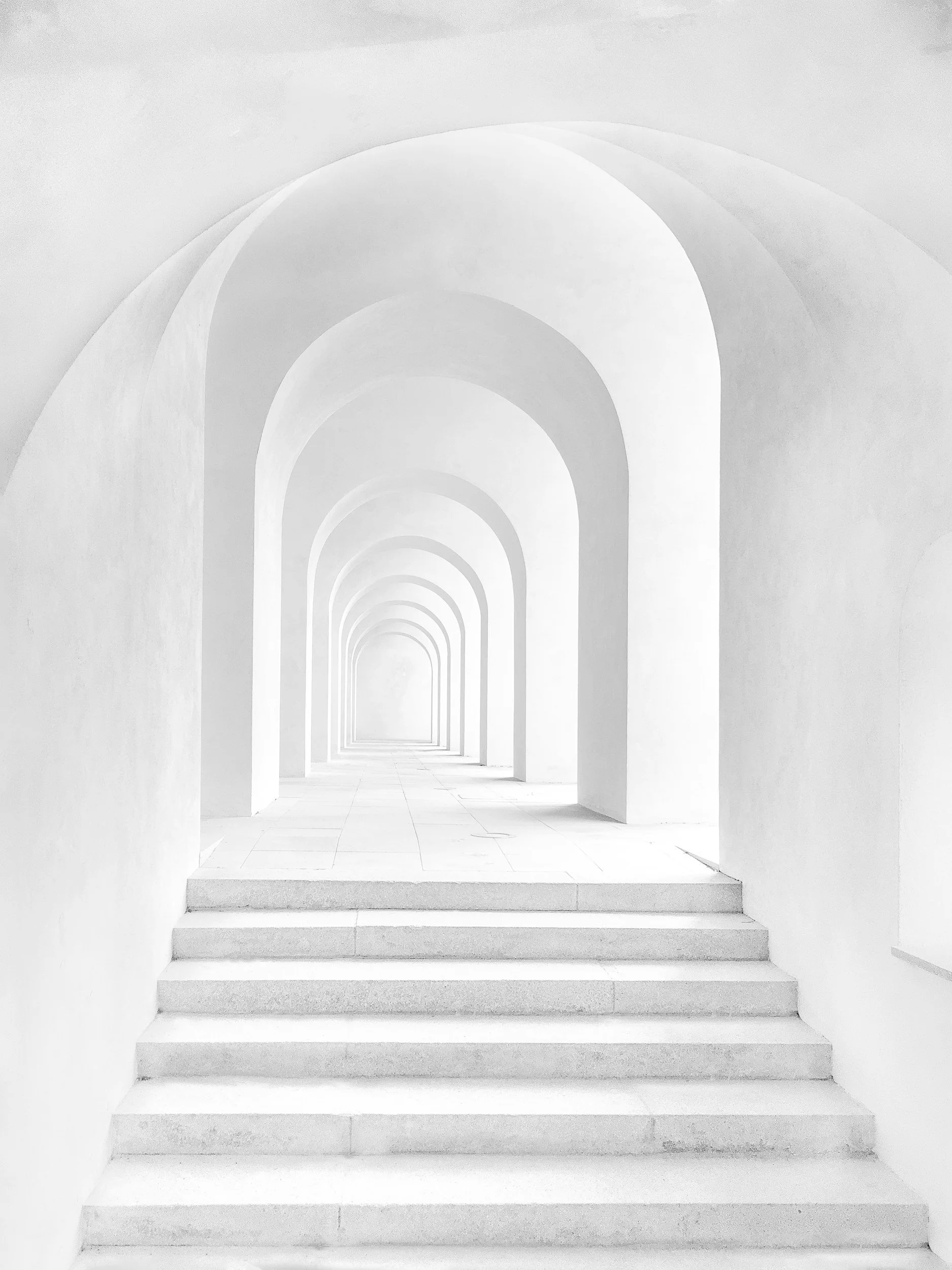 A series of white concrete steps leading up to arched doorways, creating a tunnel-like corridor with repetitive arches that recede into the distance.