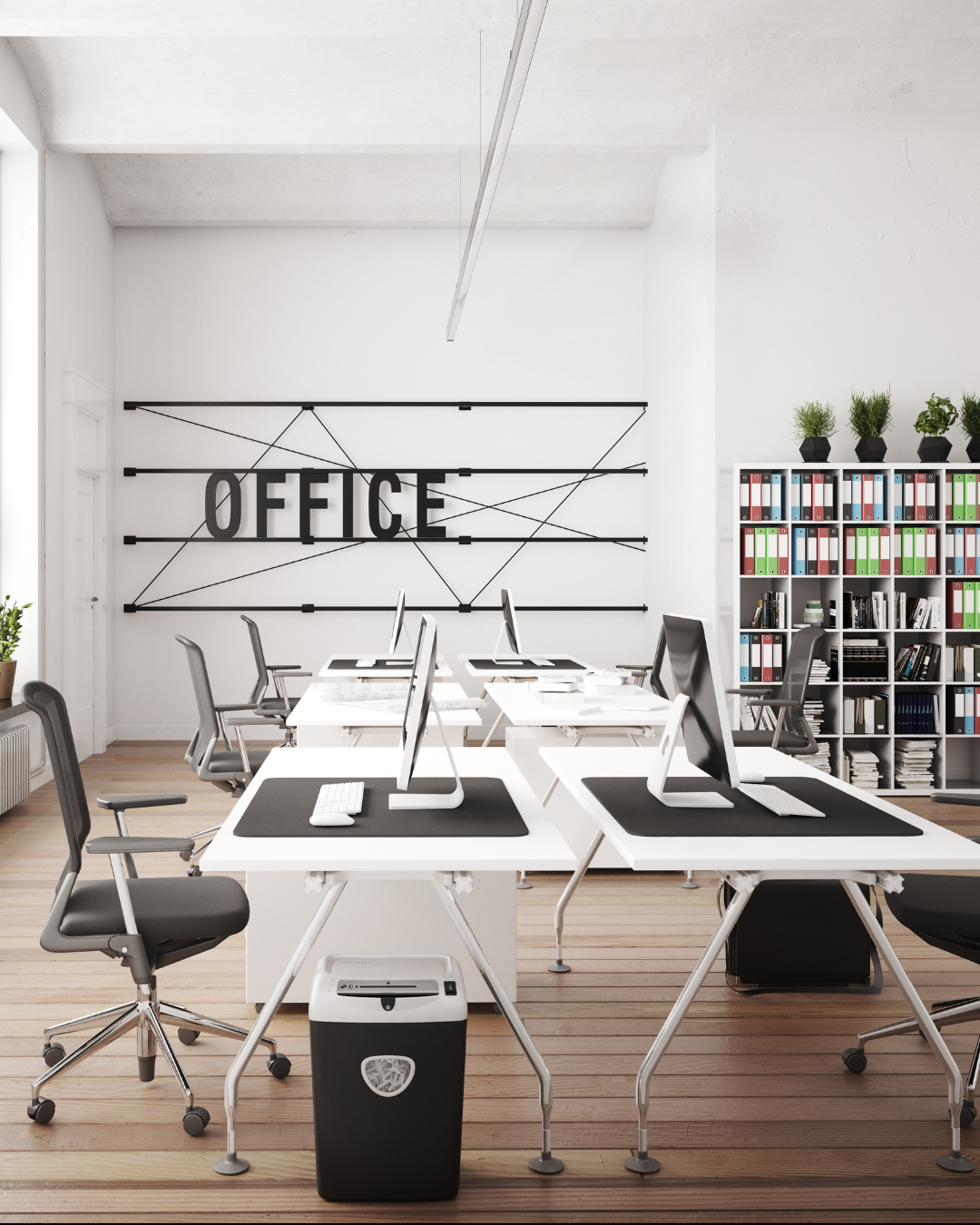 Modern office workspace with white desks, black chairs, computer monitors, and a bookshelf filled with binders and books. A large sign on the wall reads "OFFICE" in black letters.