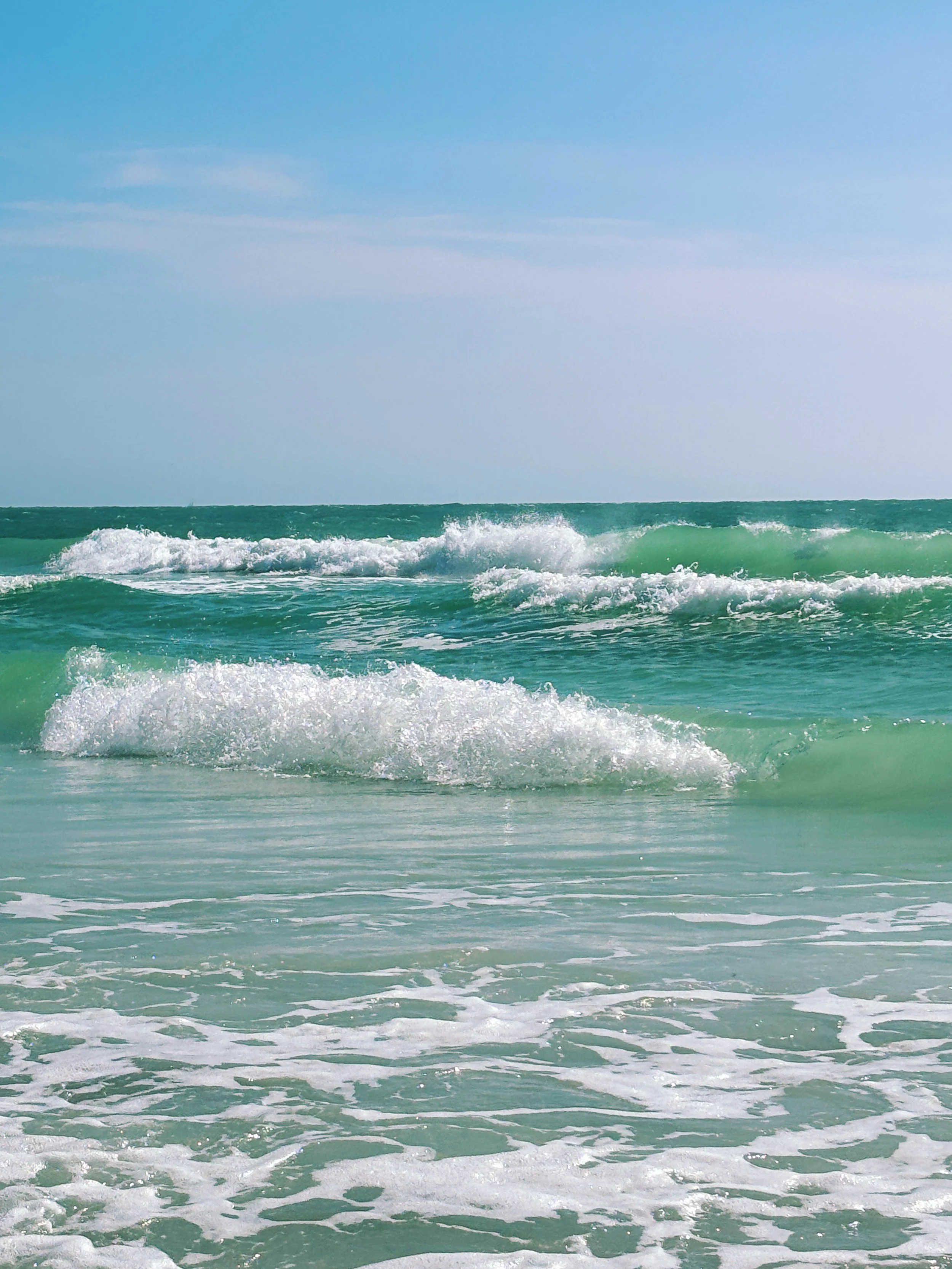 Ocean waves rolling onto the sandy shore under a partly cloudy sky.